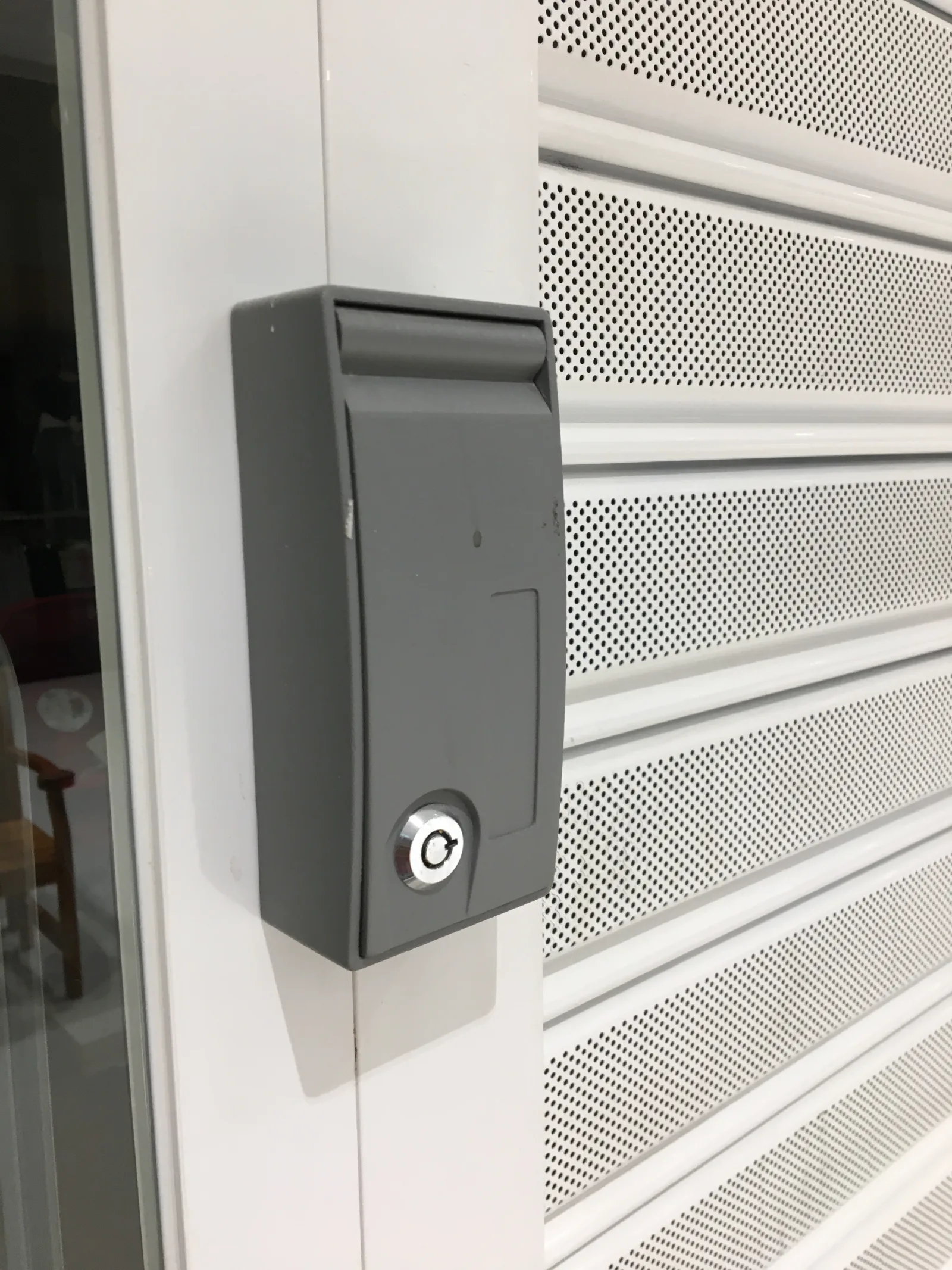 Fechadura de desbloqueio por chave numa grade de enrolar branca automatizada, para abertura manual — Grupo KEFE, Luanda.