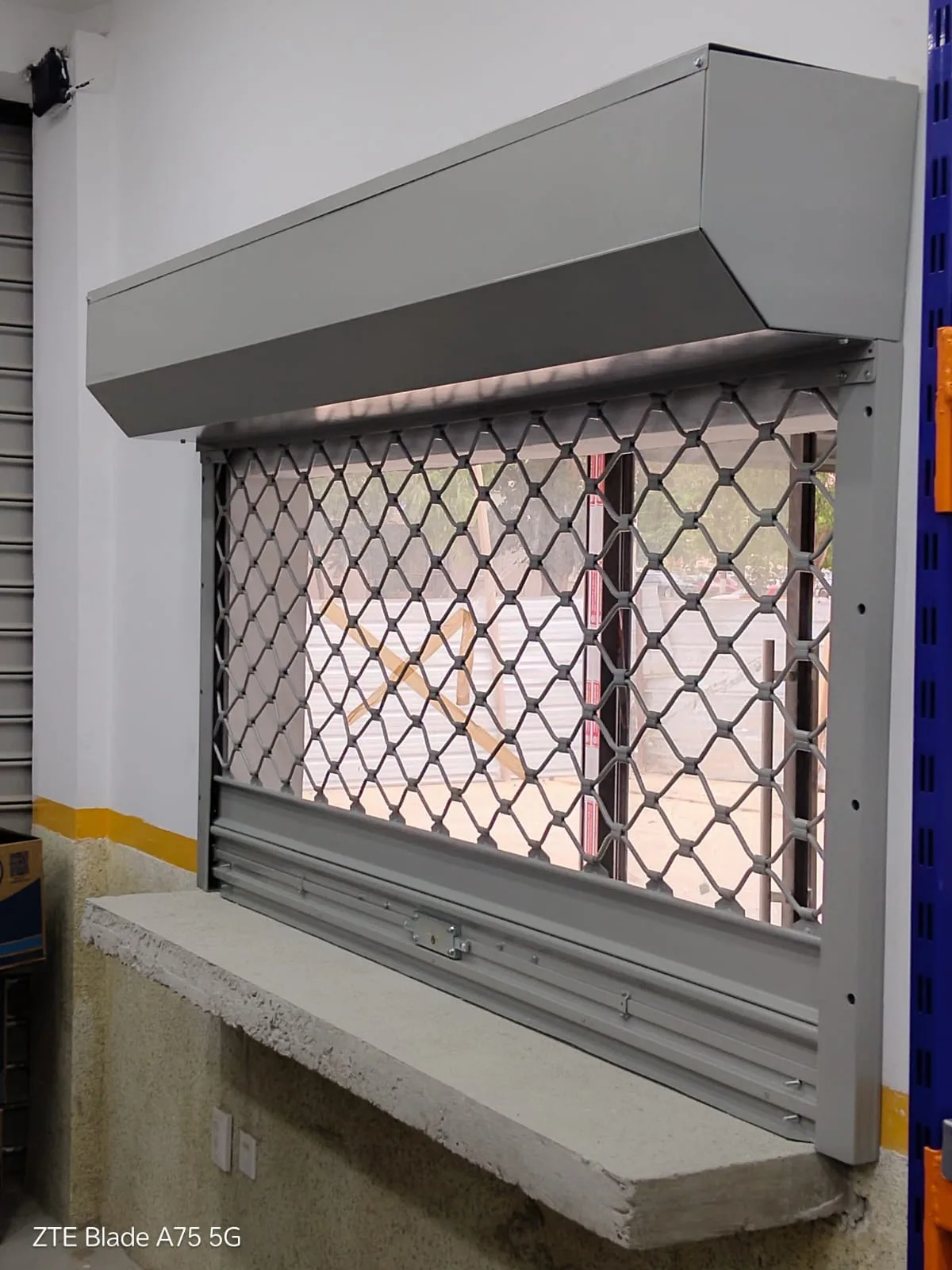 Grade de enrolar tipo lagarto, em malha de elos cinzenta, instalada sobre um balcão de atendimento — Grupo KEFE, Luanda.