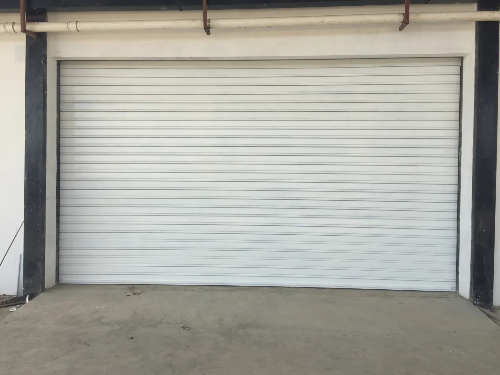 Grade de enrolar cega branca, fechada, à entrada de uma garagem — Grupo KEFE, Luanda.