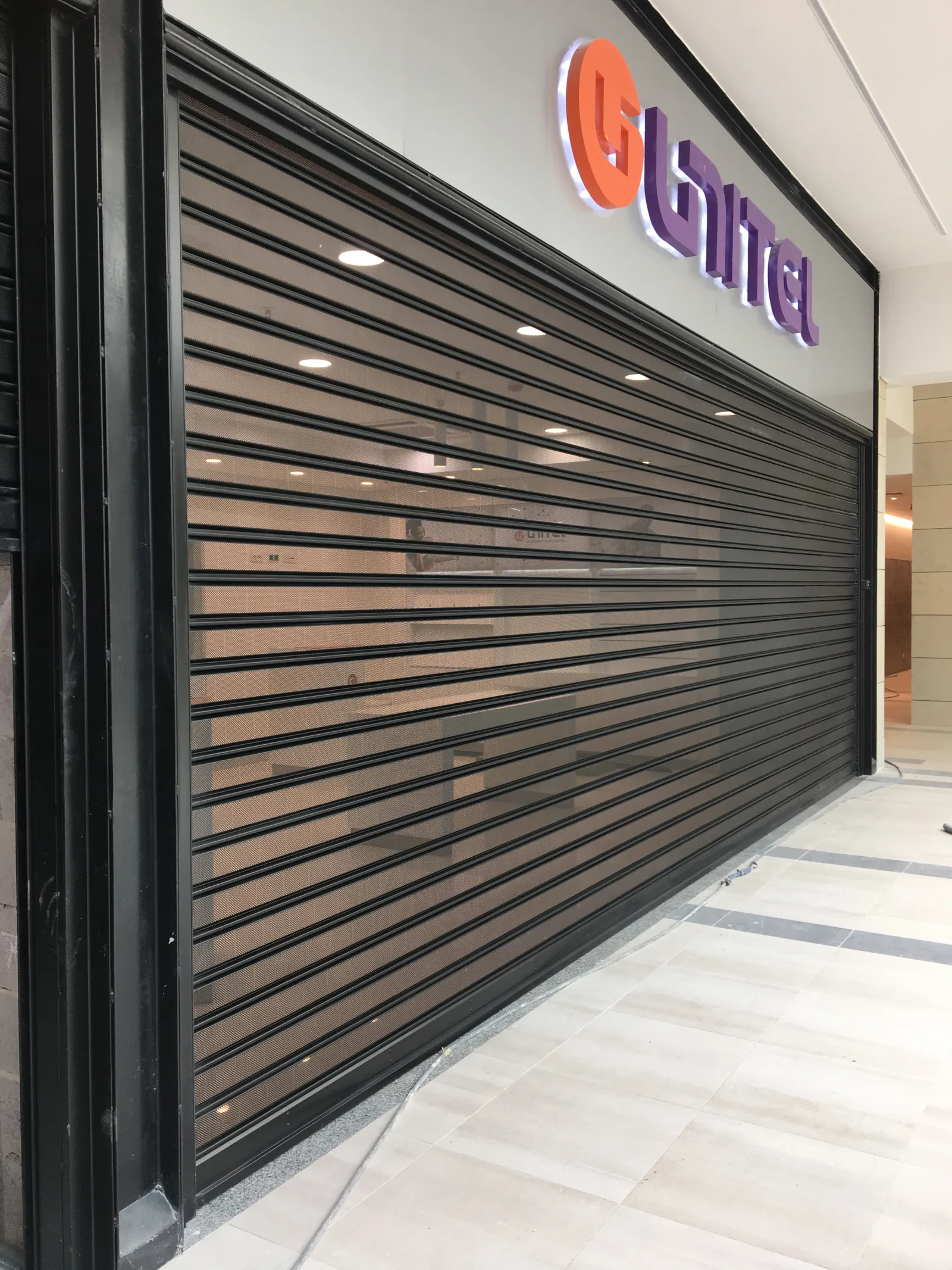 Grade de enrolar micro-perfurada, com visibilidade para o interior, numa loja Unitel — Grupo KEFE, Luanda.