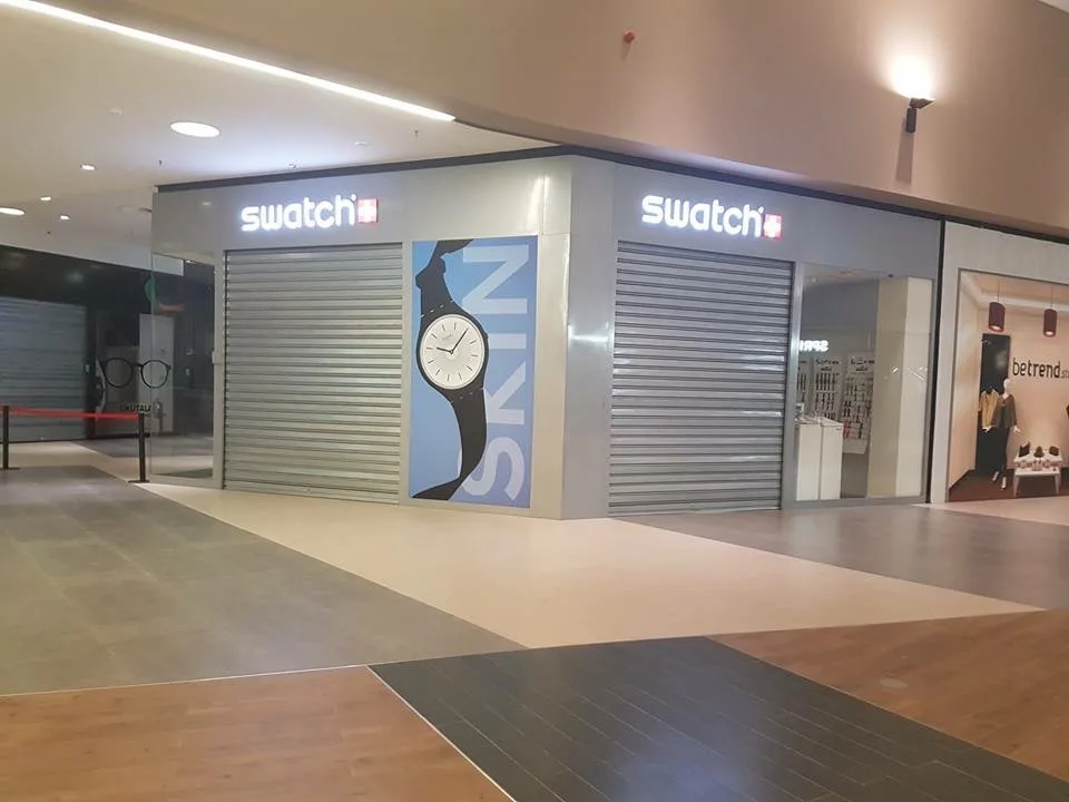 Grades de enrolar cegas cinzentas, fechadas, numa loja Swatch num centro comercial — Grupo KEFE, Luanda.