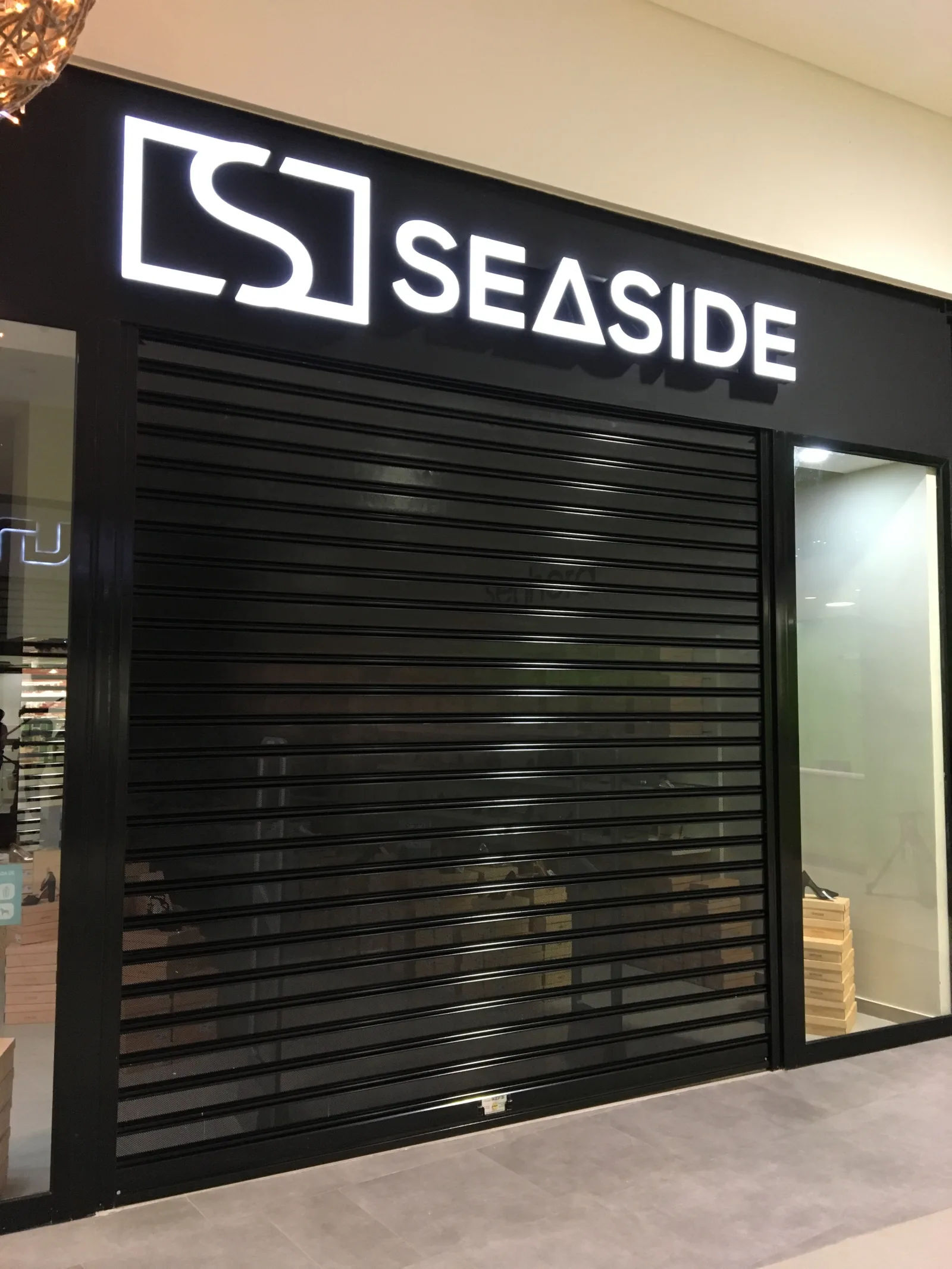 Grade de enrolar cega preta, fechada, numa loja Seaside num centro comercial — Grupo KEFE, Luanda.