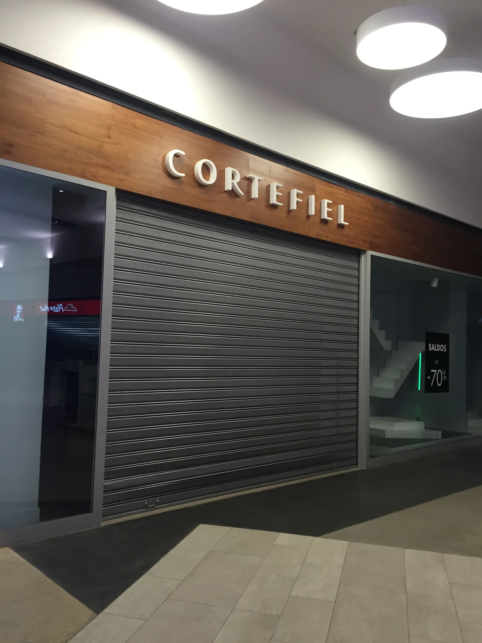 Grade de enrolar cega cinzenta, fechada, numa loja Cortefiel num centro comercial — Grupo KEFE, Luanda.