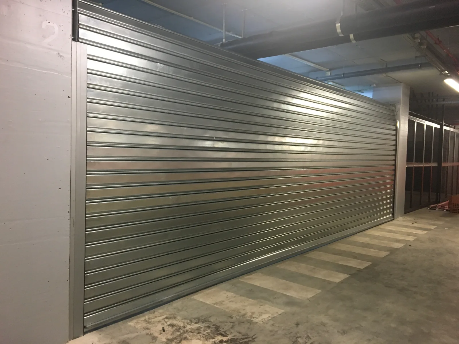 Grade de enrolar cega em aço galvanizado, de grande dimensão, numa zona de estacionamento — Grupo KEFE, Luanda.