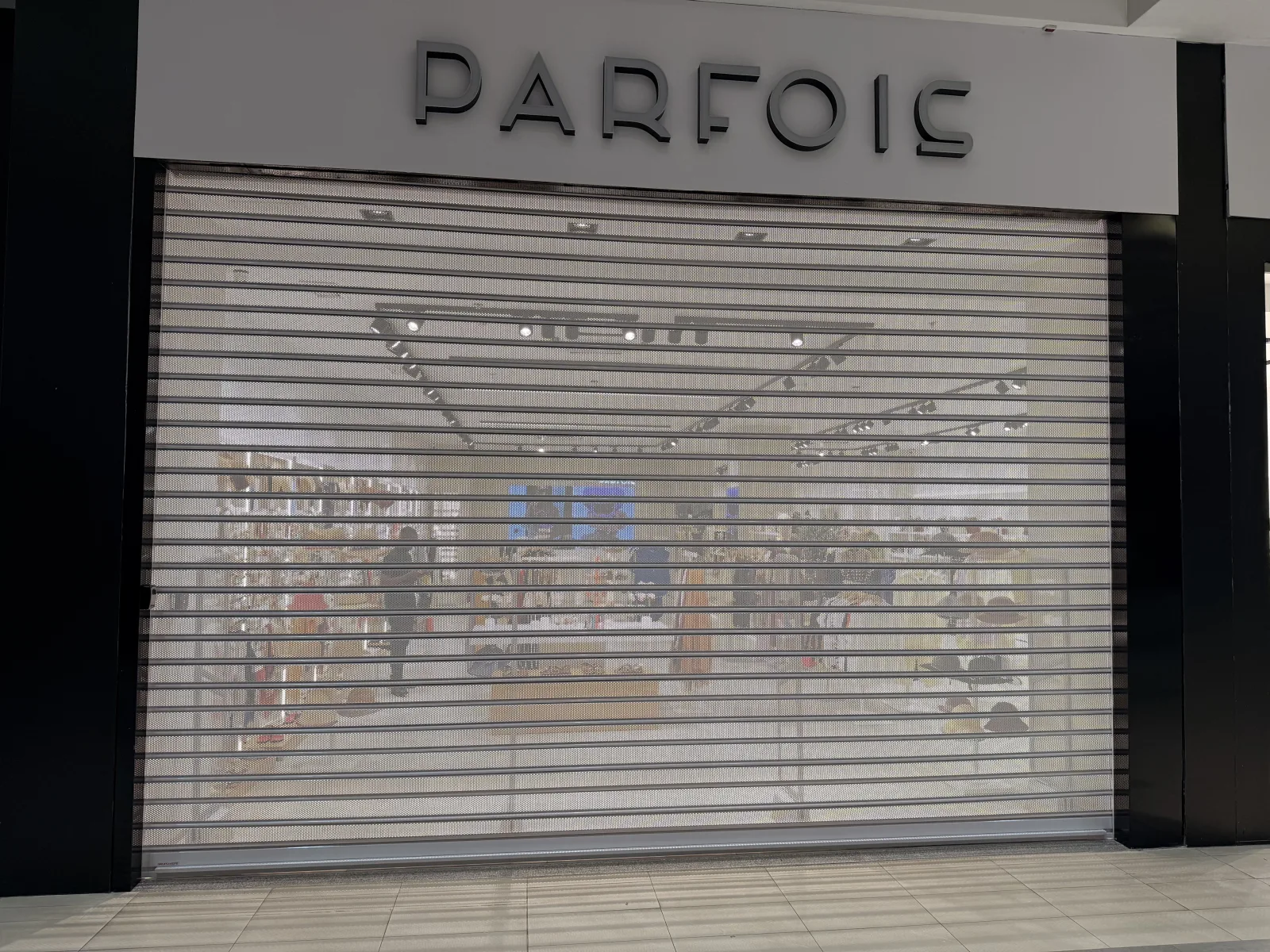 Grade de enrolar micro-perfurada, semiaberta, à entrada da loja Parfois num centro comercial — Grupo KEFE, Luanda.
