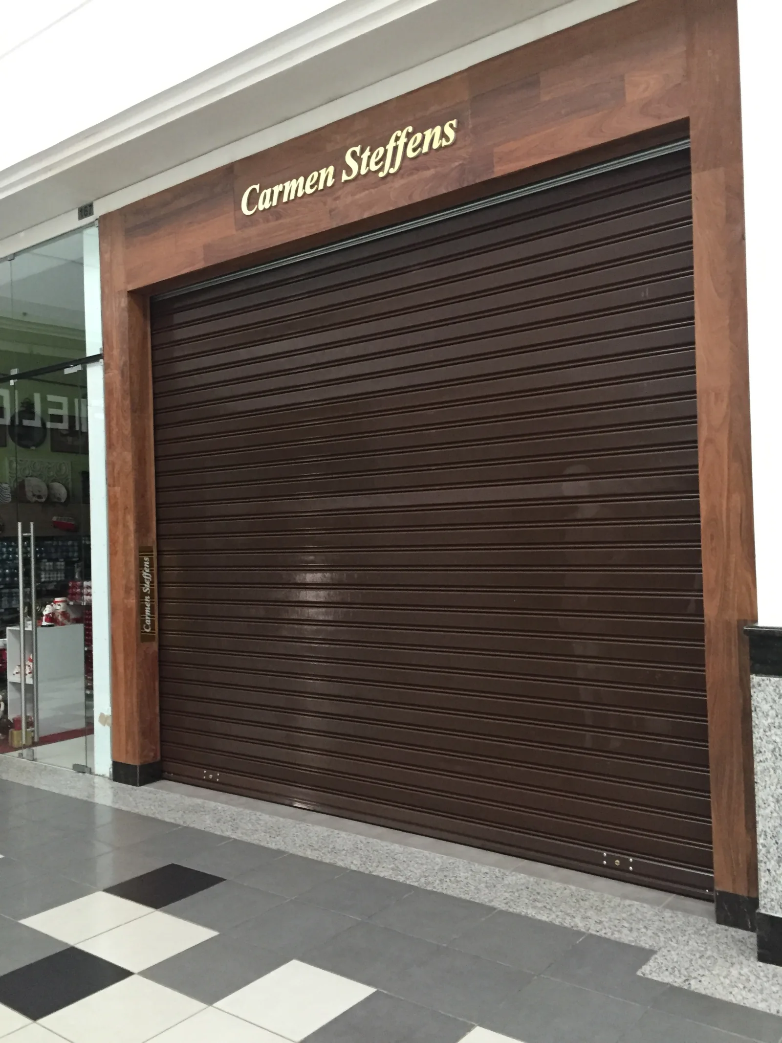 Grade de enrolar cega castanha (imitação madeira), fechada, numa loja Carmen Steffens num centro comercial — Grupo KEFE, Luanda.