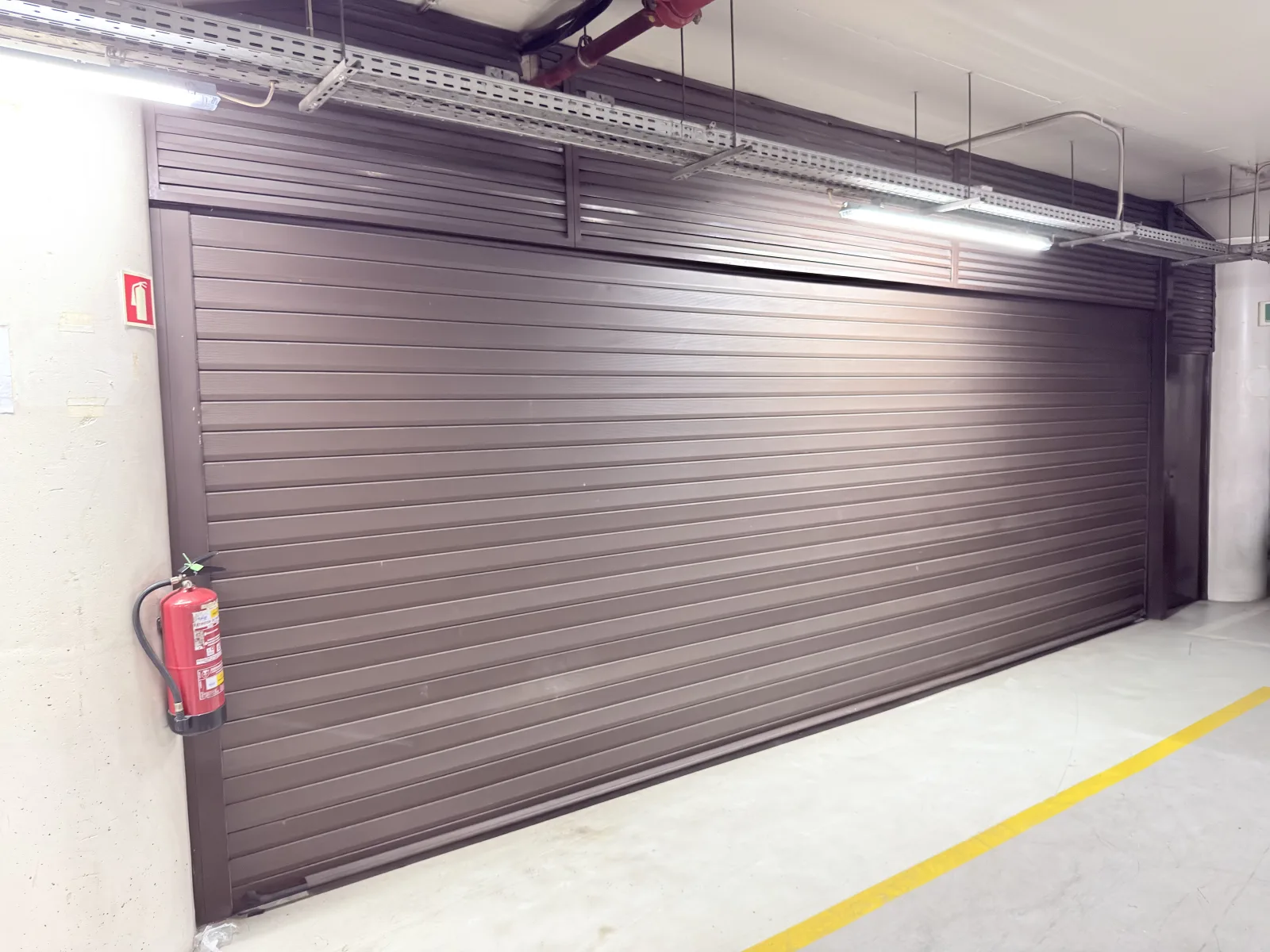 Porta de enrolar castanha de grande dimensão, fechada, numa garagem coberta — Grupo KEFE, Luanda.