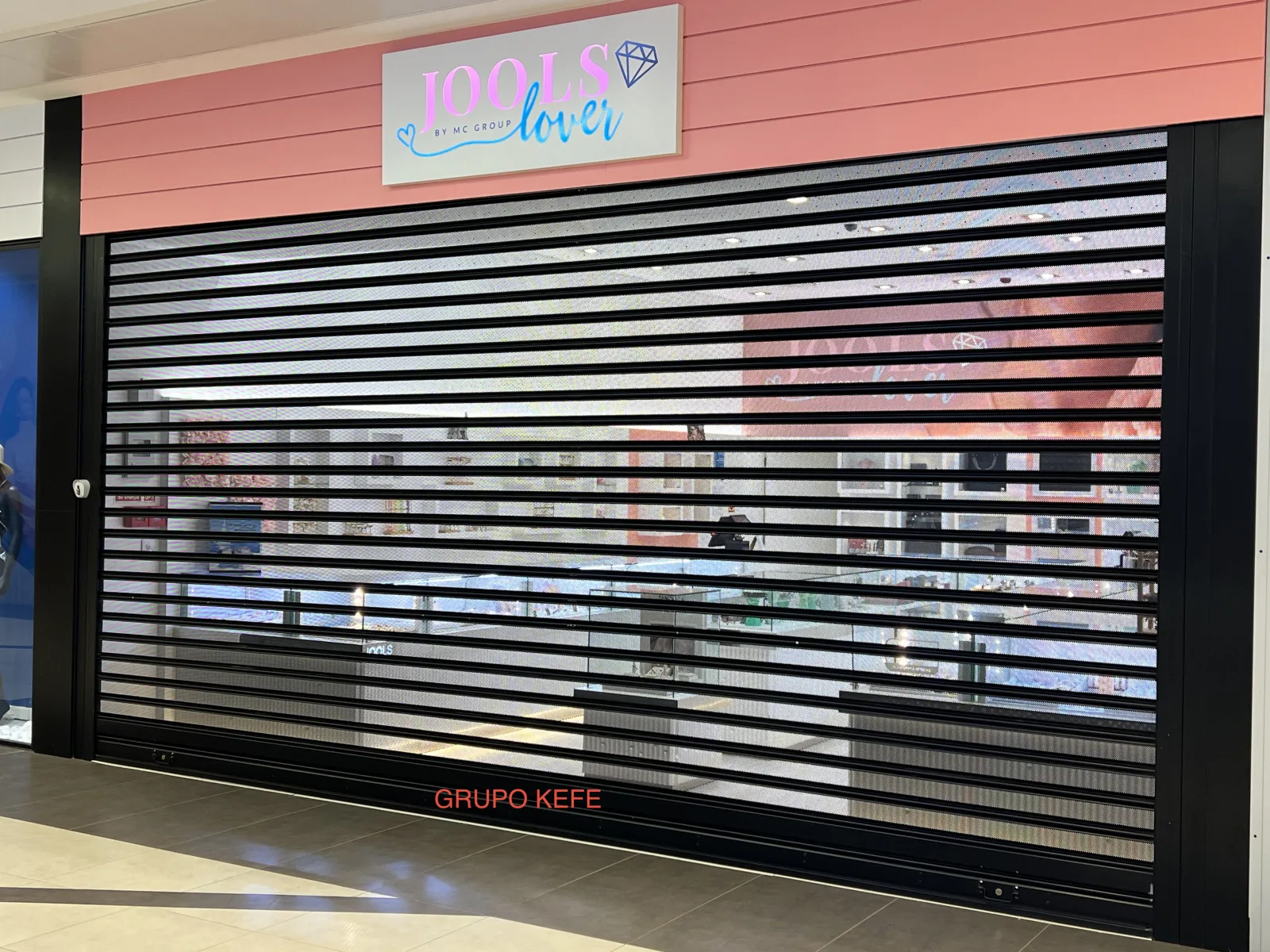 Grade de enrolar micro-perfurada preta, com visibilidade da montra, numa loja Jools Fever, com marca Grupo KEFE — Luanda.