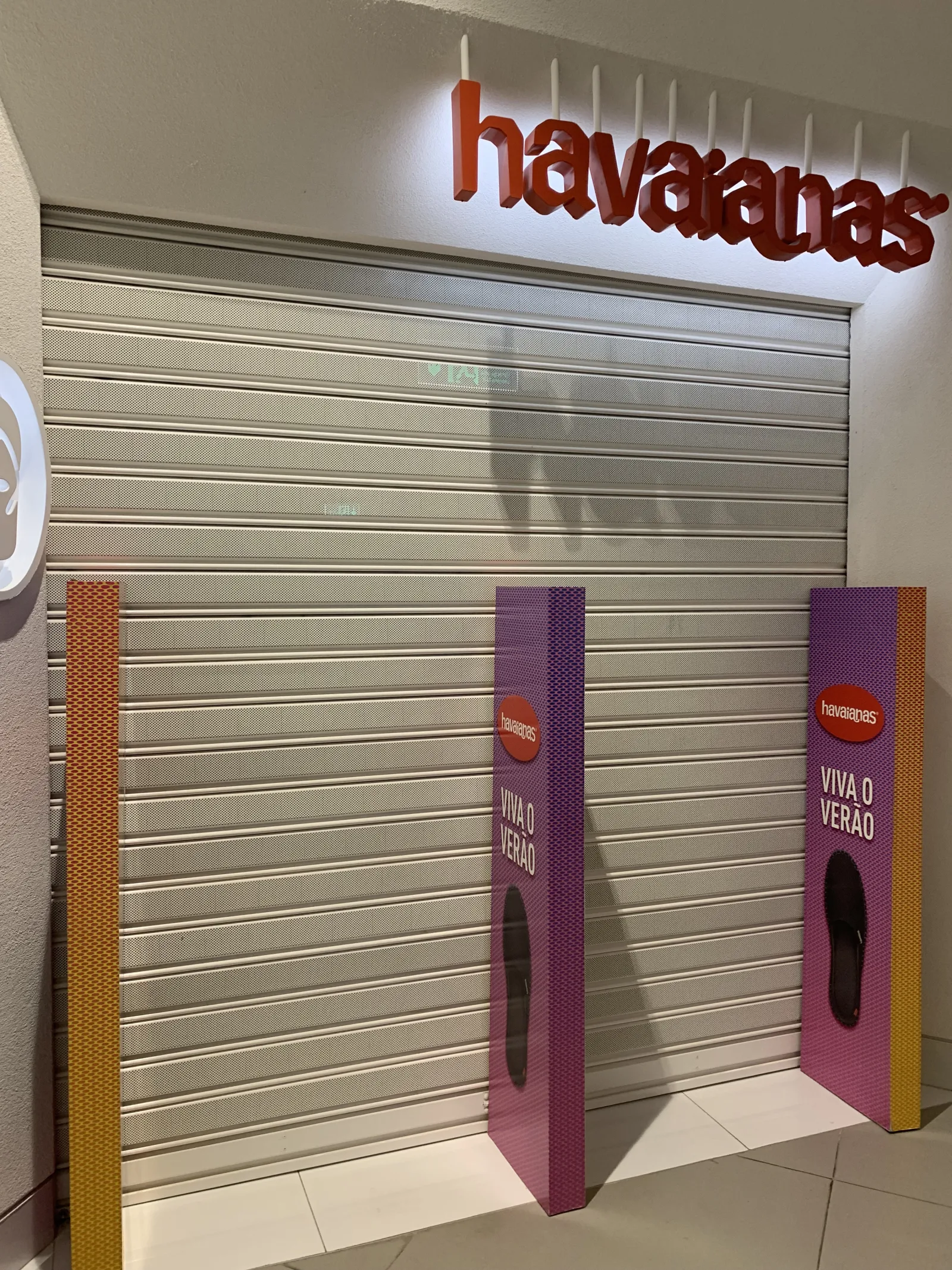 Grade de enrolar cega em tom creme, fechada, numa loja Havaianas num centro comercial — Grupo KEFE, Luanda.