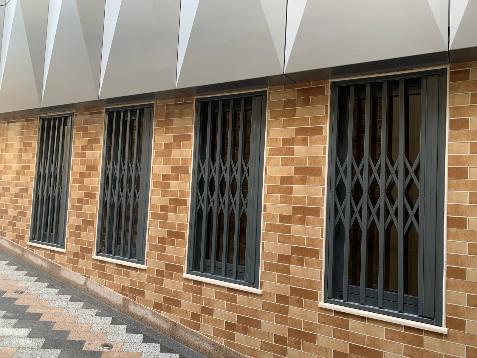 Grades lagarto cinzentas extensíveis em janelas de um edifício de tijolo — Grupo KEFE, Luanda.