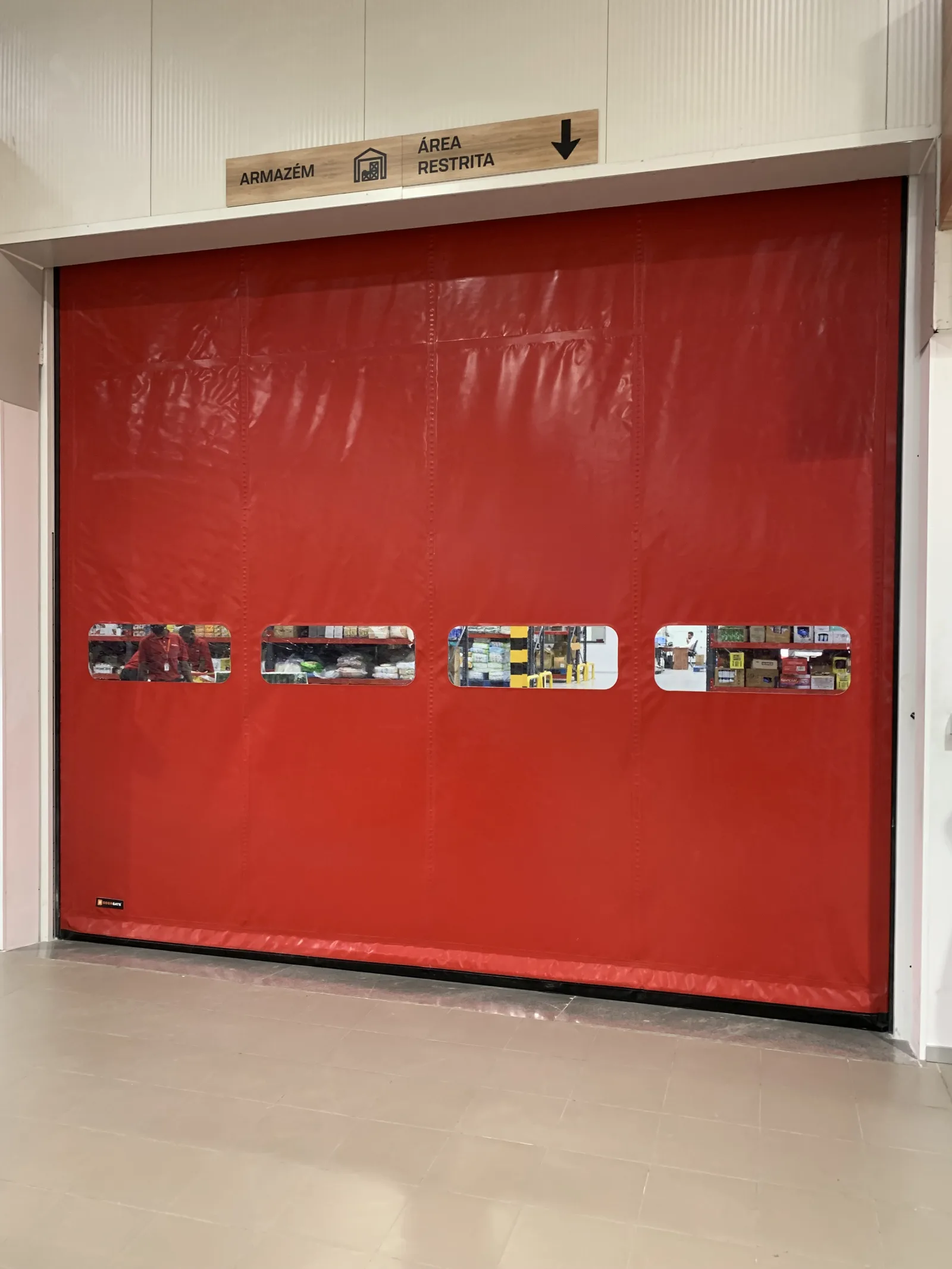 Porta rápida de lona vermelha, com janela de visão, num acesso interior de armazém — Grupo KEFE, Luanda.