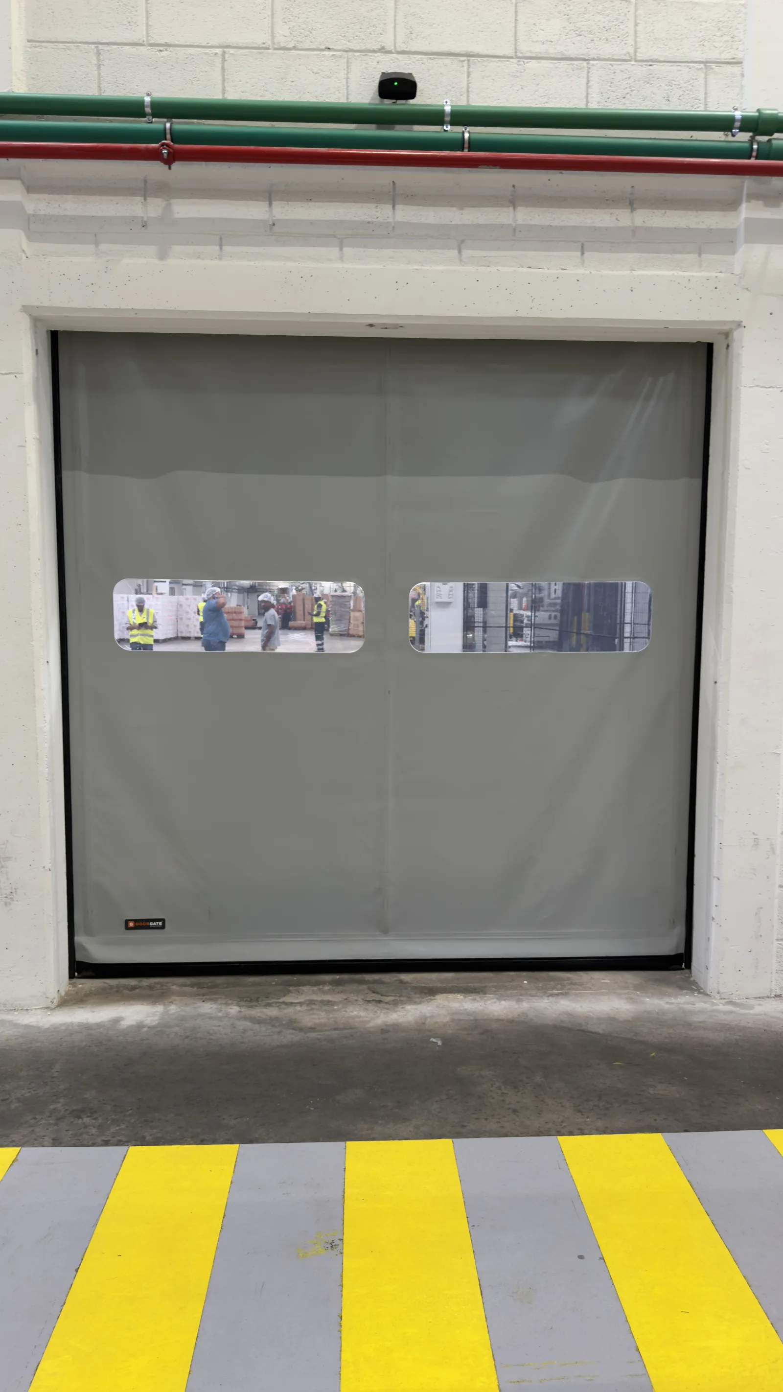 Porta rápida de lona cinzenta, fechada, num vão industrial com marcações de segurança no piso — Grupo KEFE, Luanda.