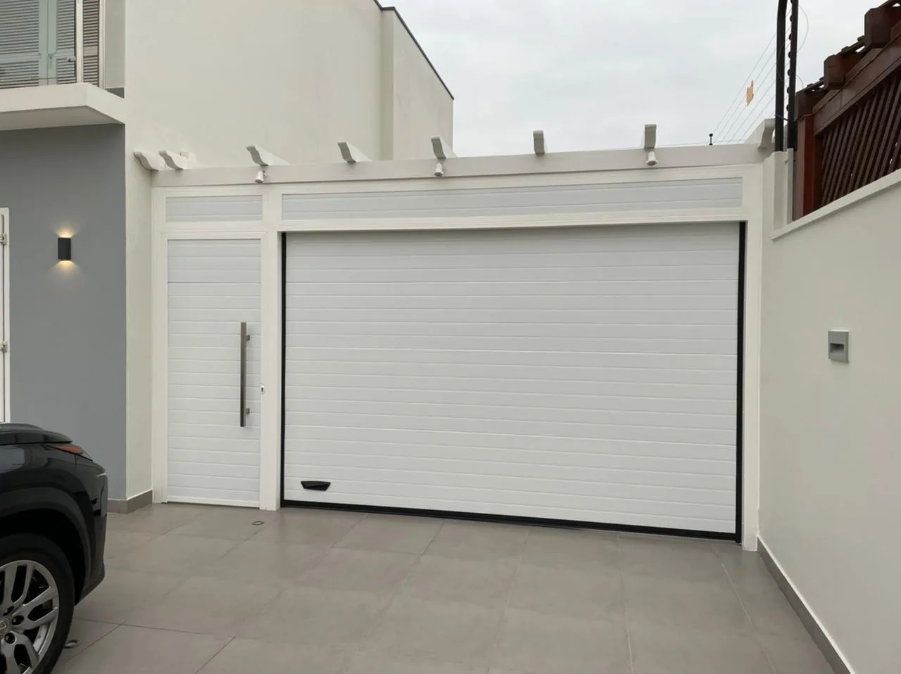 Portão seccionado branco de painéis frisados com porta lateral a condizer, numa moradia