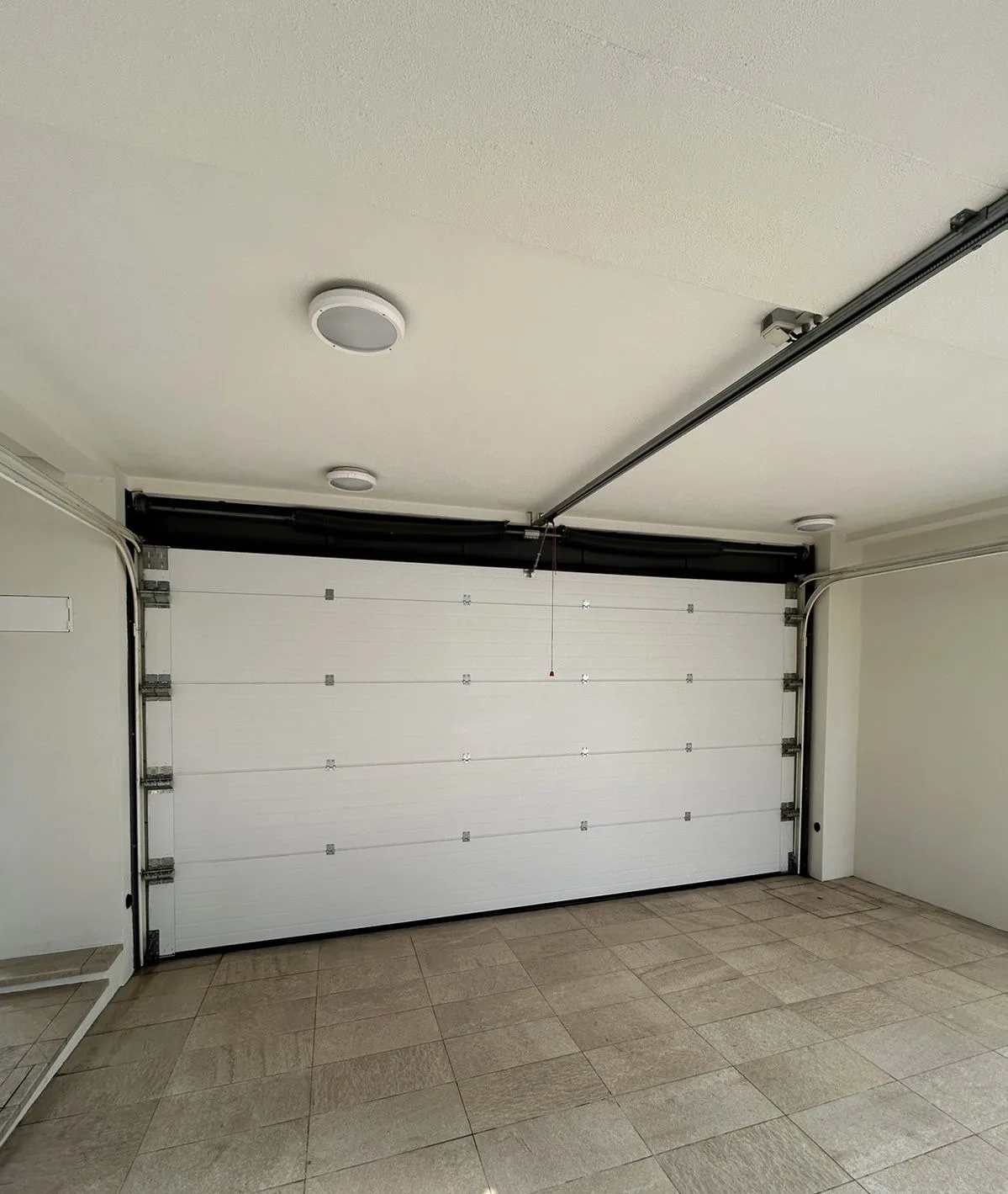 Portão seccionado branco visto do interior da garagem, com veio de molas e calhas no teto