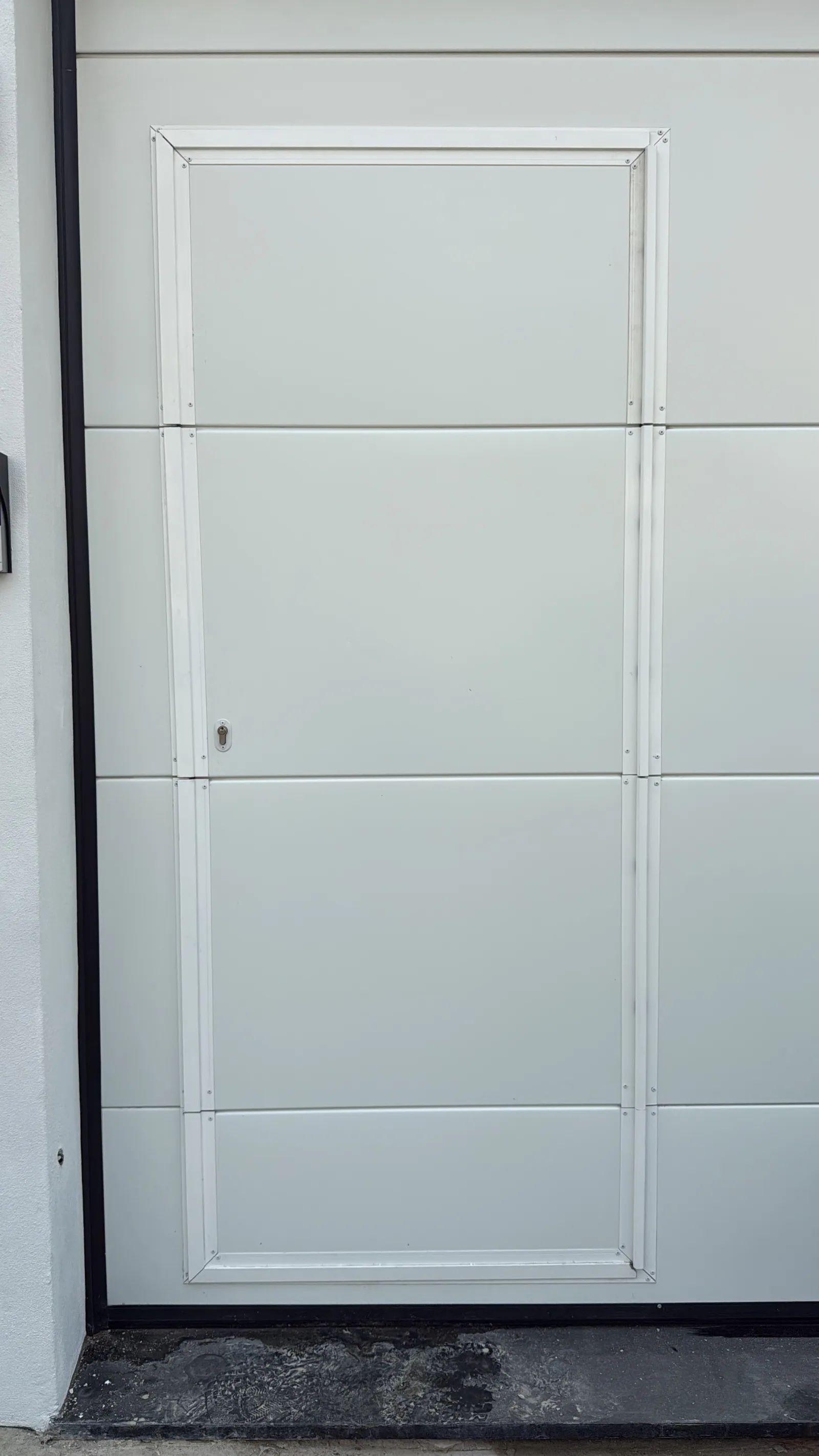 Pormenor de porta de serviço (postigo) integrada num portão seccionado branco de painéis lisos