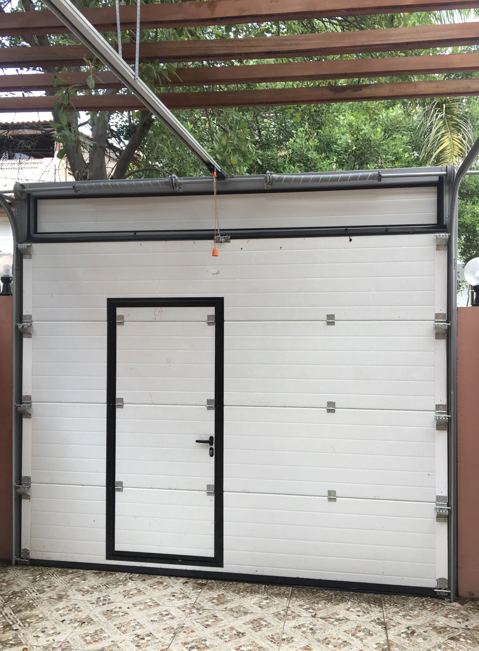Portão seccionado branco com postigo de moldura preta, com calhas e molas visíveis durante a instalação