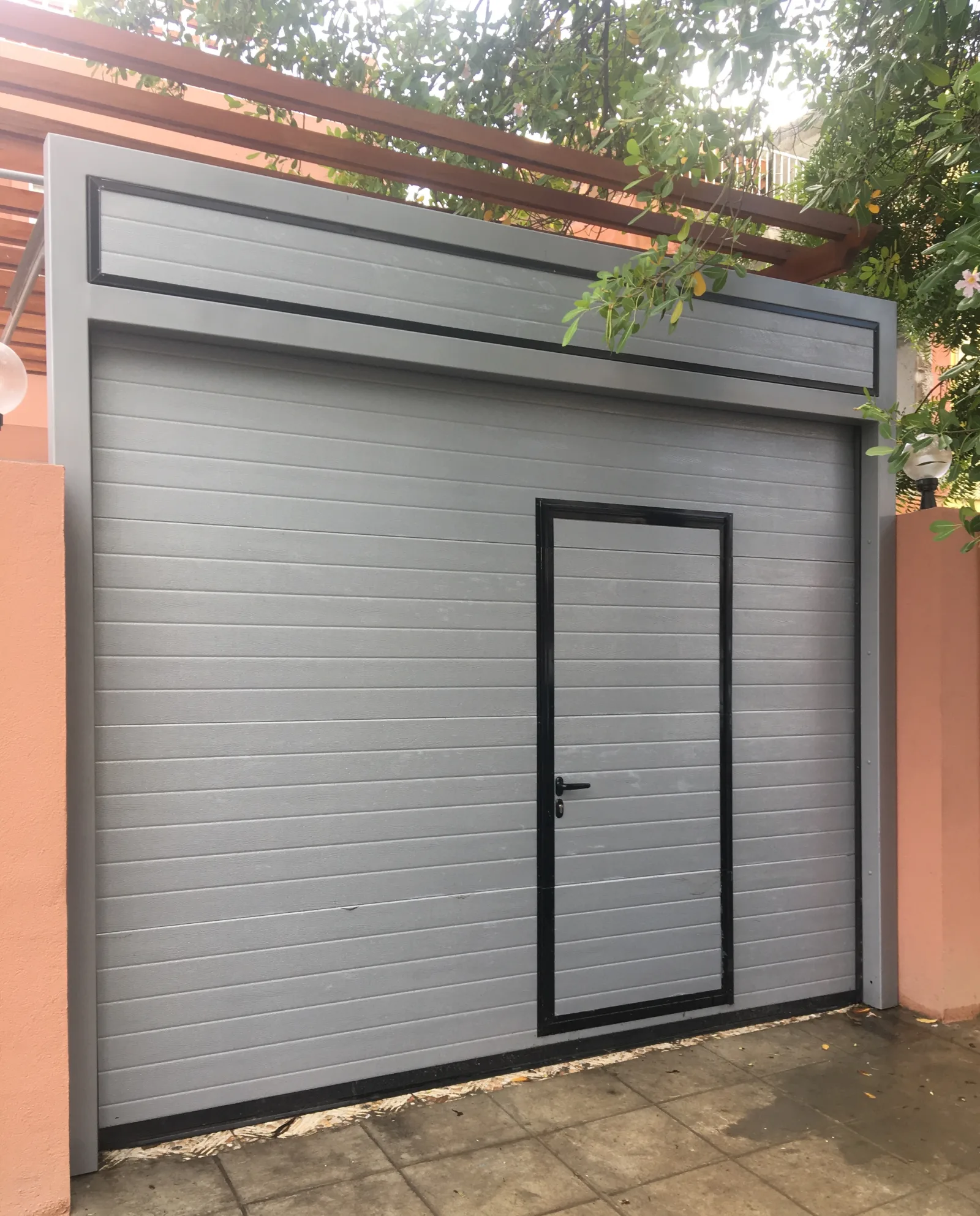 Portão seccionado cinzento com porta de serviço integrada na garagem de uma moradia