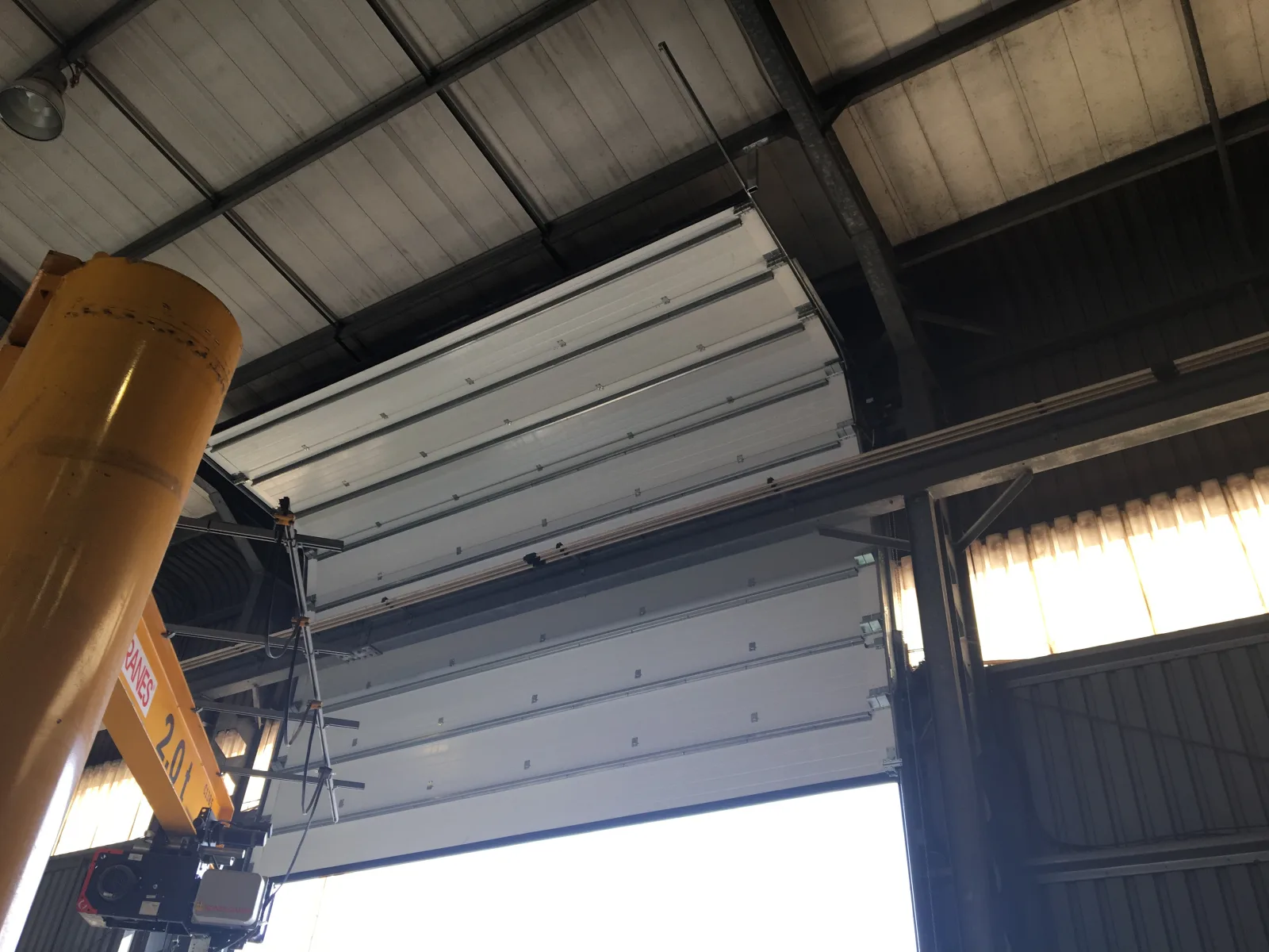 Painéis brancos de um portão seccionado recolhidos ao longo das calhas, junto ao teto de uma nave industrial