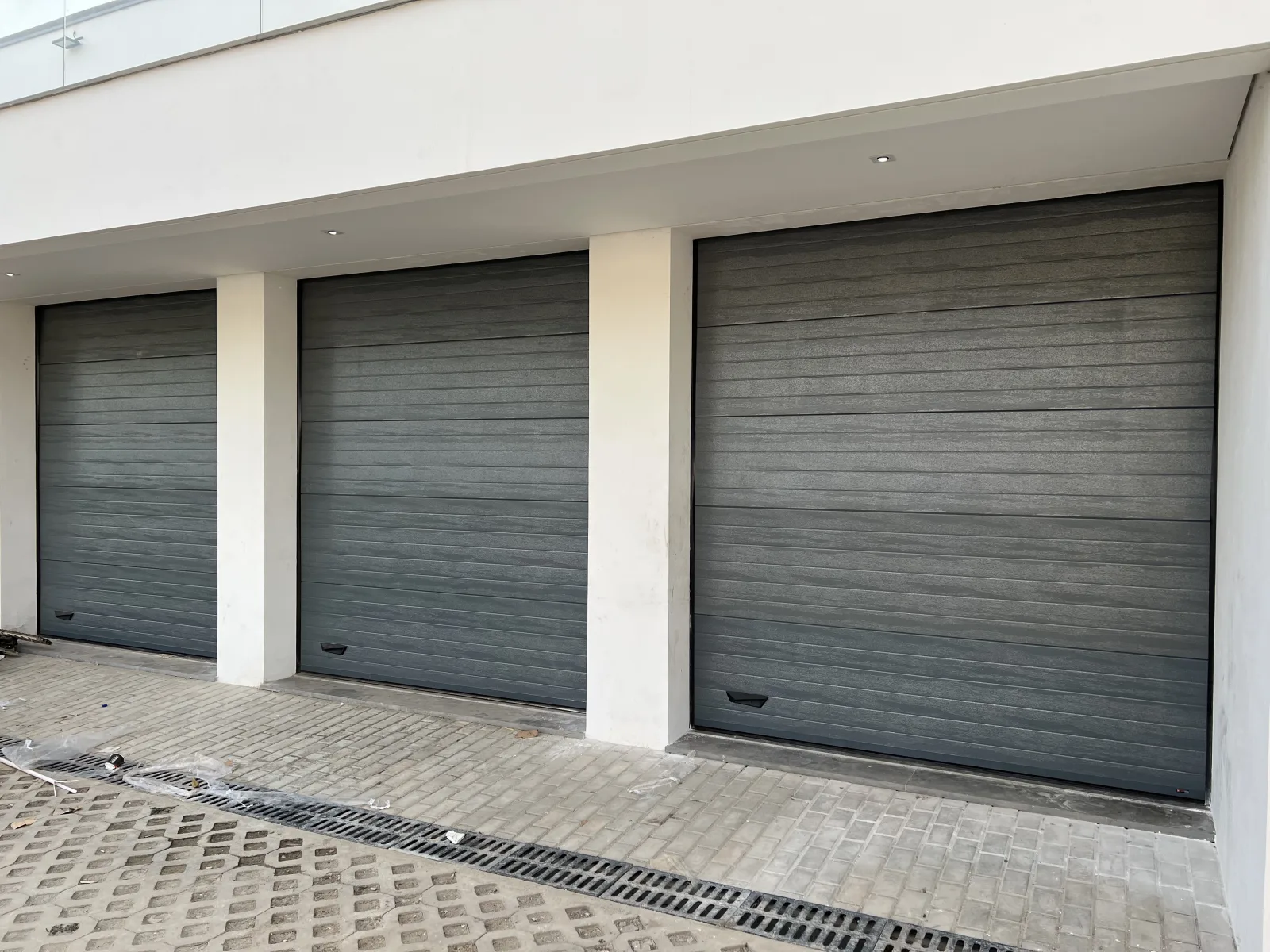 Três portões seccionados em cinzento-escuro lado a lado nas garagens de um condomínio