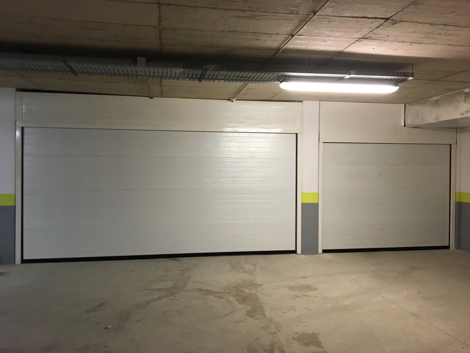 Dois portões seccionados brancos numa garagem coletiva interior