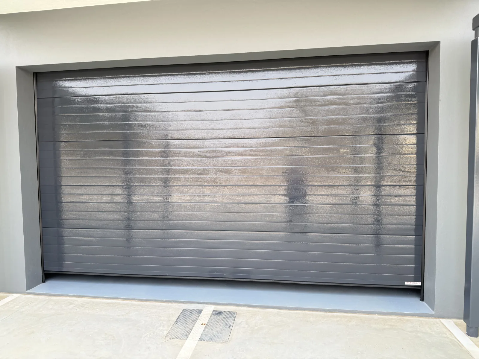 Portão seccionado cinzento-escuro de painéis frisados na garagem de uma moradia