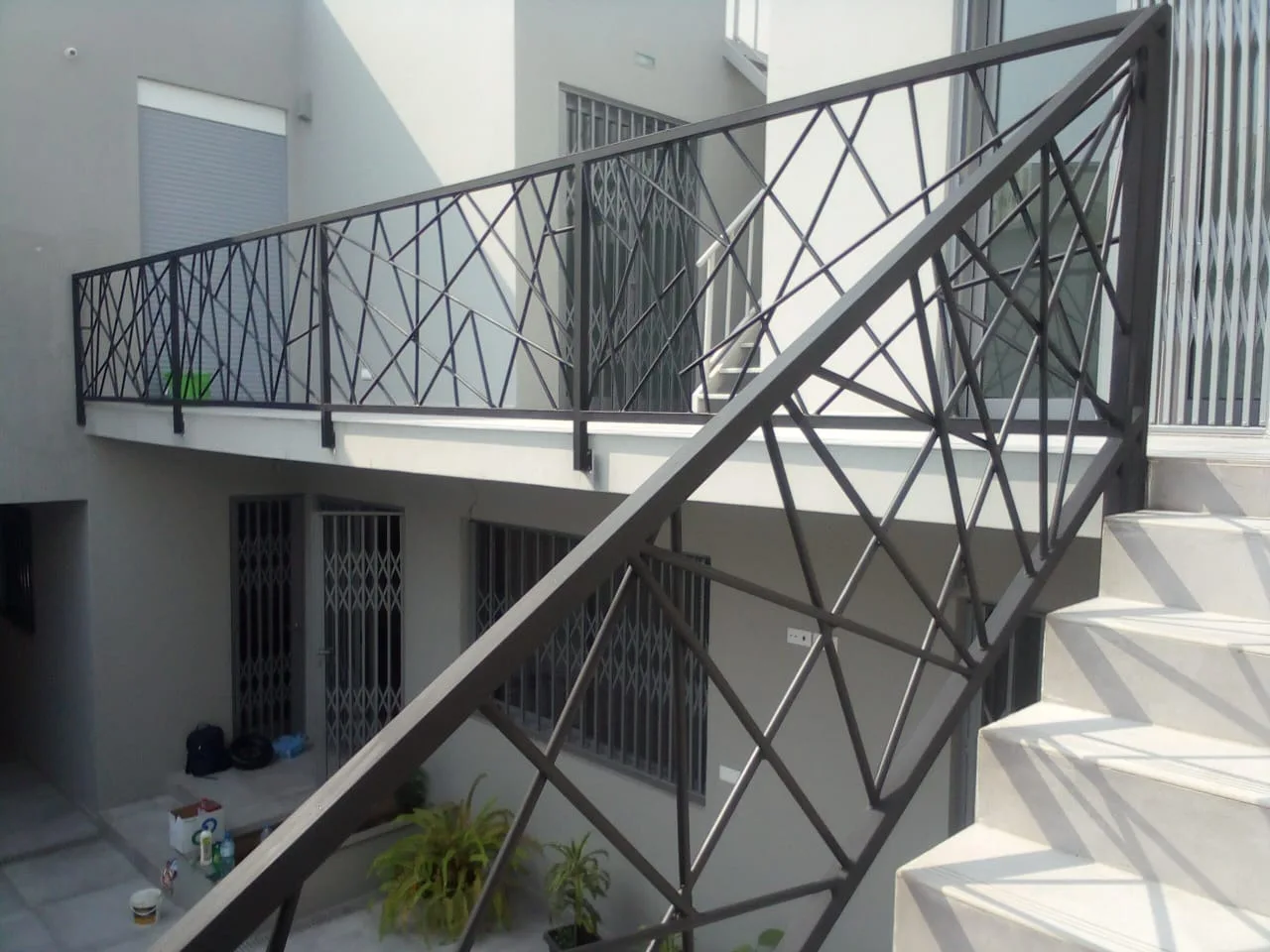 Guarda-corpos metálico preto com padrão de barras cruzadas, numa escada exterior de um edifício — Grupo KEFE, Luanda.
