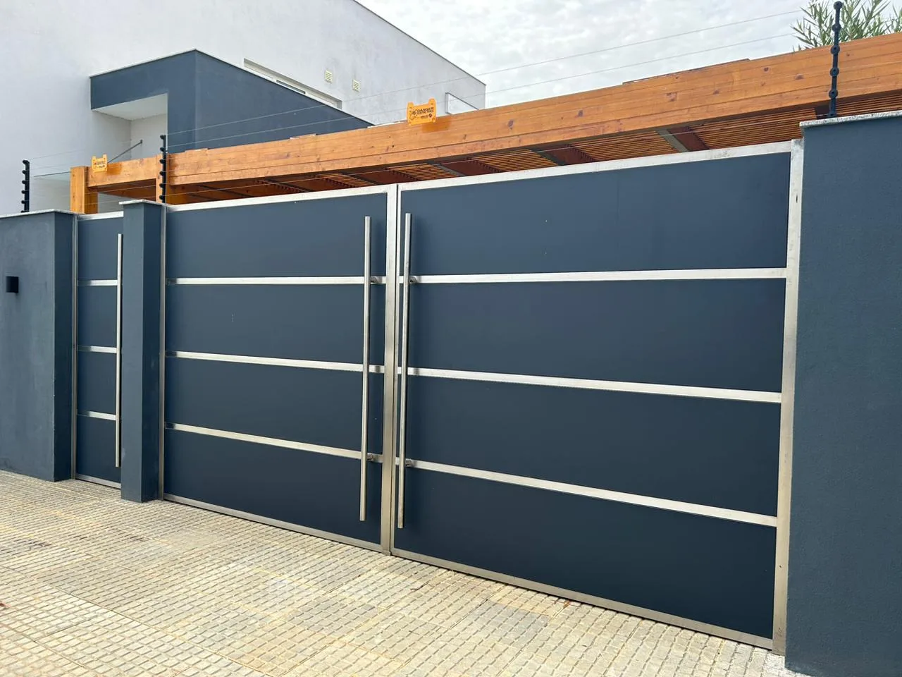 Portão de correr azul-acinzentado com frisos horizontais de inox, numa moradia — Grupo KEFE, Luanda.