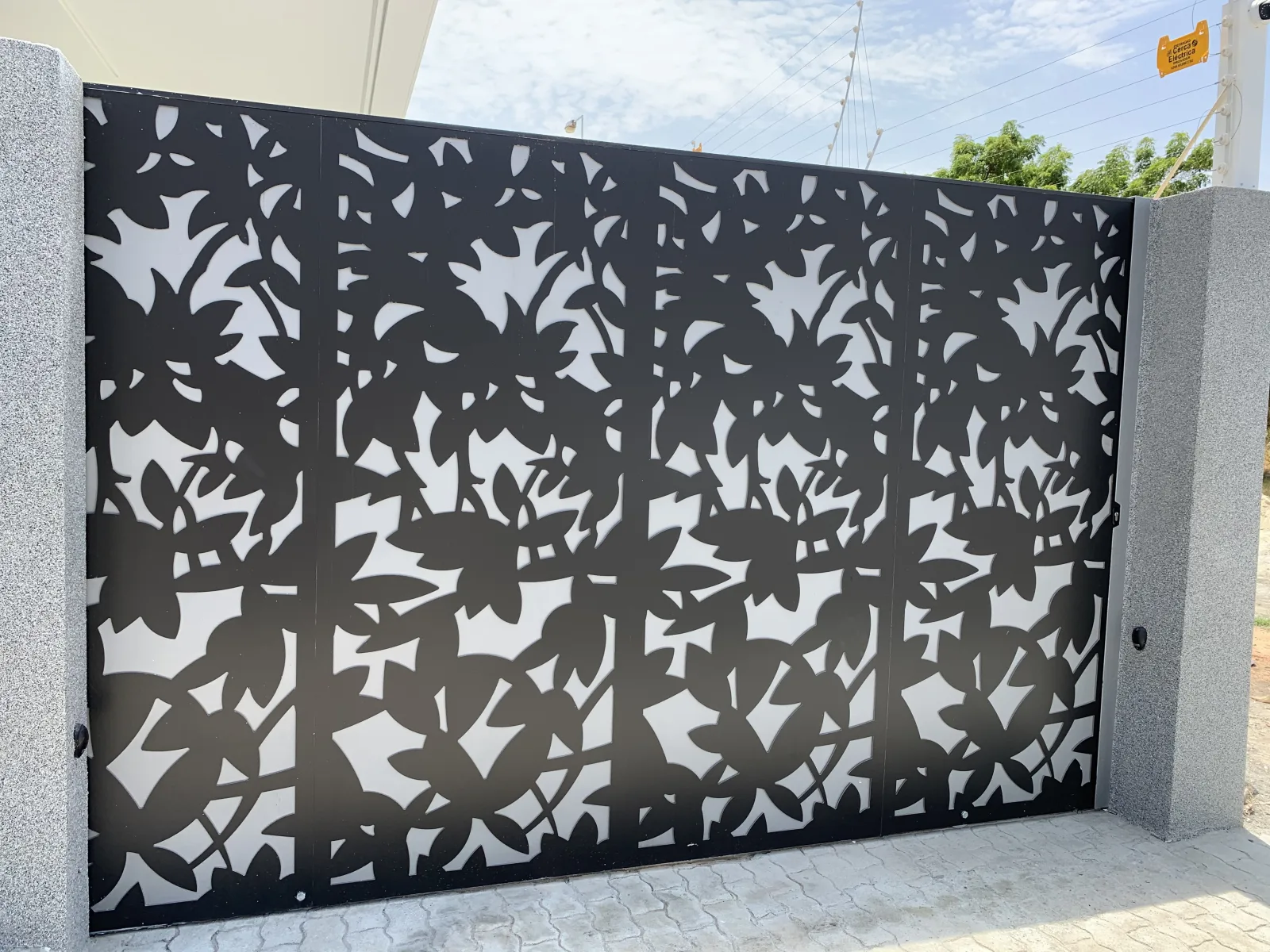 Portão decorativo em chapa metálica recortada a laser com padrão de folhagem, à entrada de uma moradia — Grupo KEFE, Luanda.