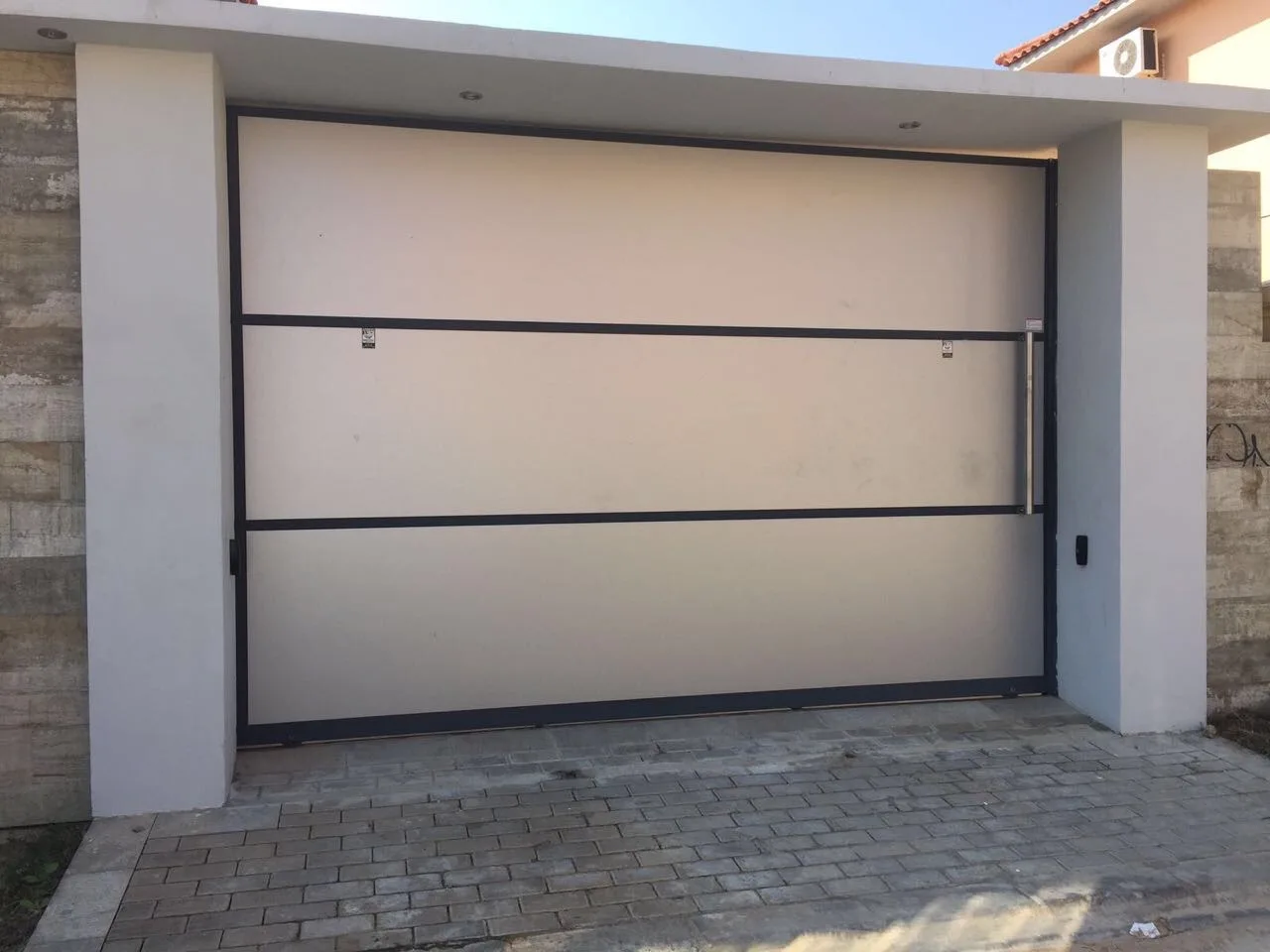 Portão de garagem seccionado, bege, com friso envidraçado, numa moradia moderna — Grupo KEFE, Luanda.