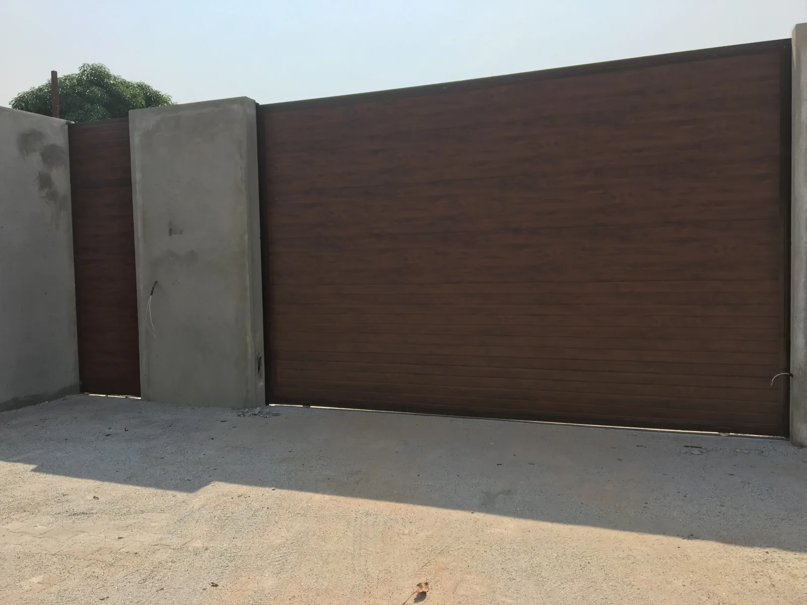 Portão de correr com acabamento imitação de madeira, à entrada de um lote — Grupo KEFE, Luanda.