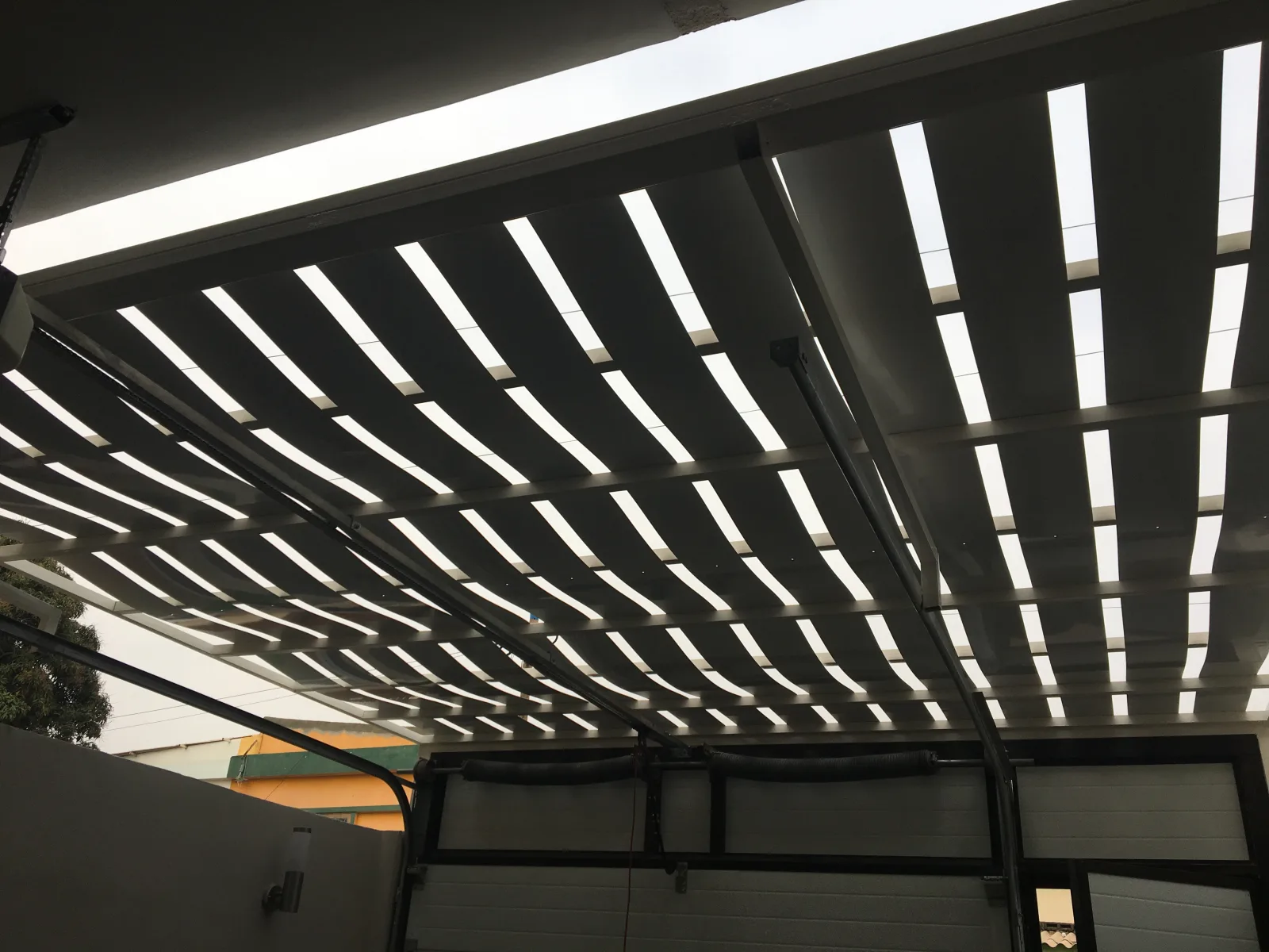 Cobertura metálica tipo pérgola, com ripado e chapa translúcida, vista por baixo — Grupo KEFE, Luanda.