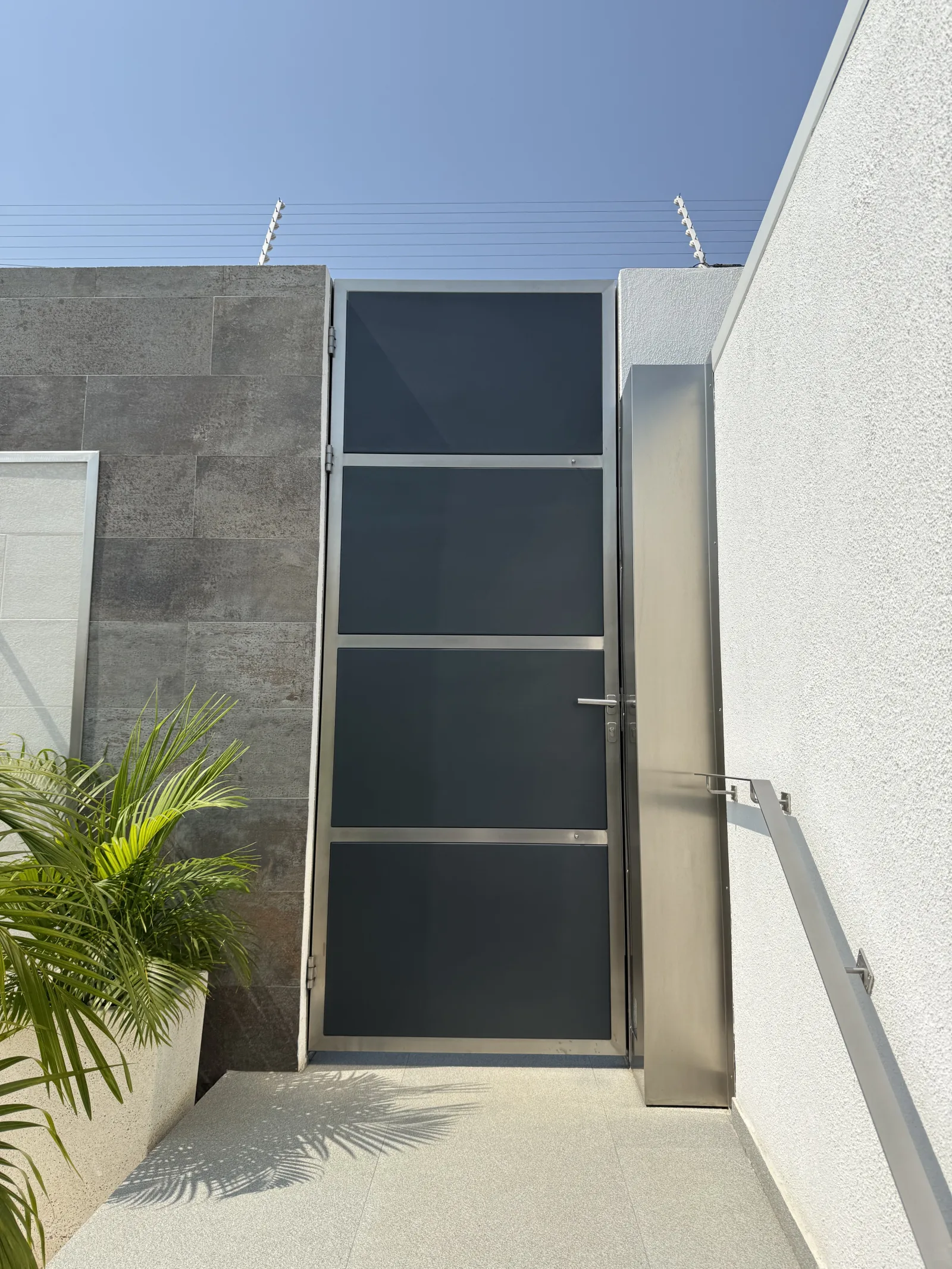 Portão pedonal estreito, em estrutura metálica e vidro fumado, num acesso lateral — Grupo KEFE, Luanda.