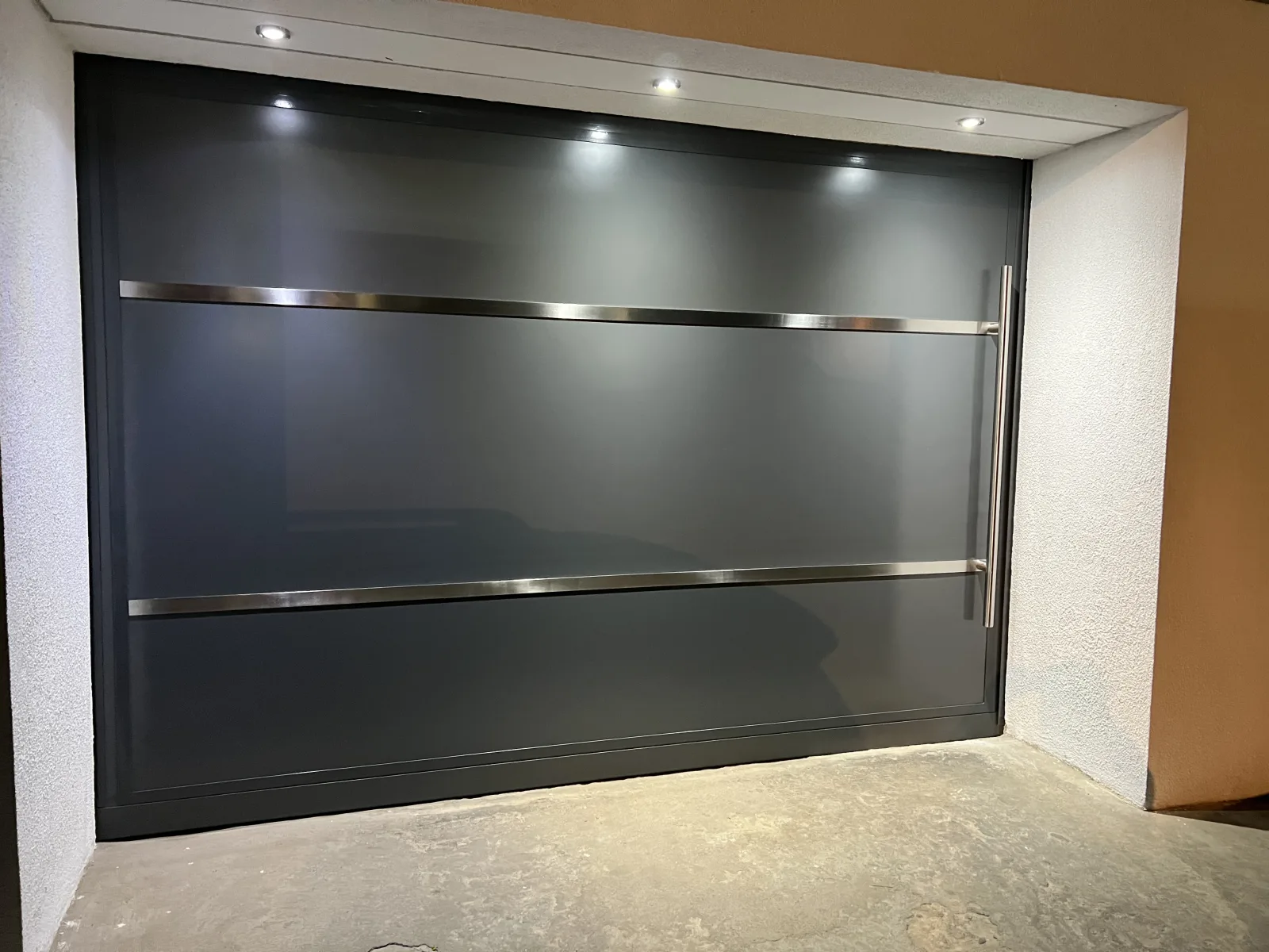 Portão de garagem escuro com frisos de inox, numa garagem com iluminação embutida — Grupo KEFE, Luanda.