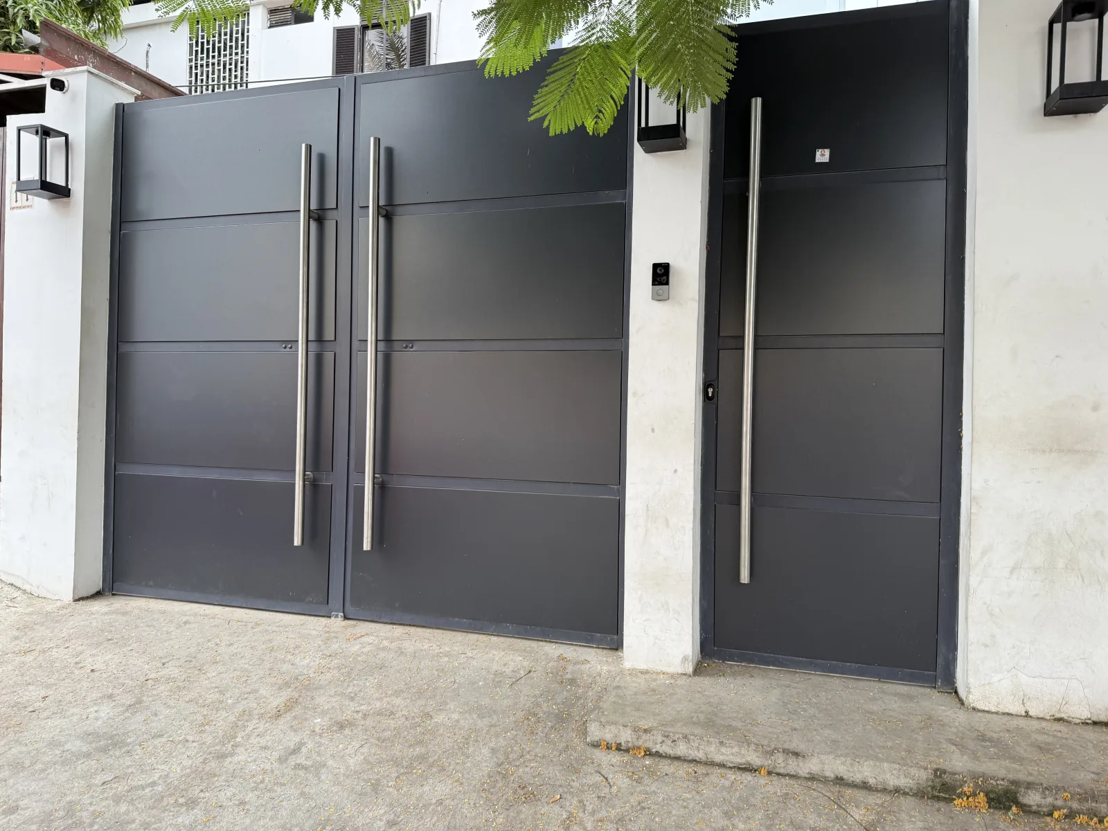 Portão de entrada alto, em chapa cinza-escuro com puxadores verticais de inox, numa moradia — Grupo KEFE, Luanda.