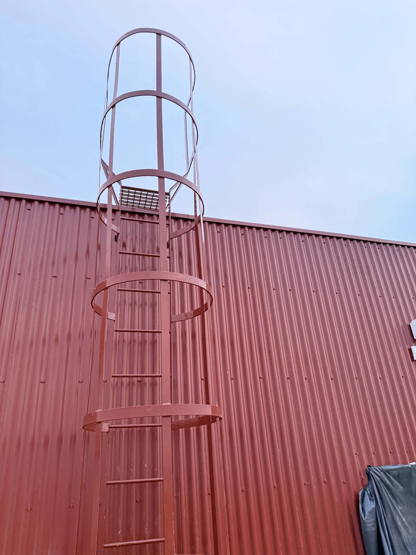Escada de marinheiro metálica com guarda-costas, fixada à parede de um pavilhão industrial — Grupo KEFE, Luanda.