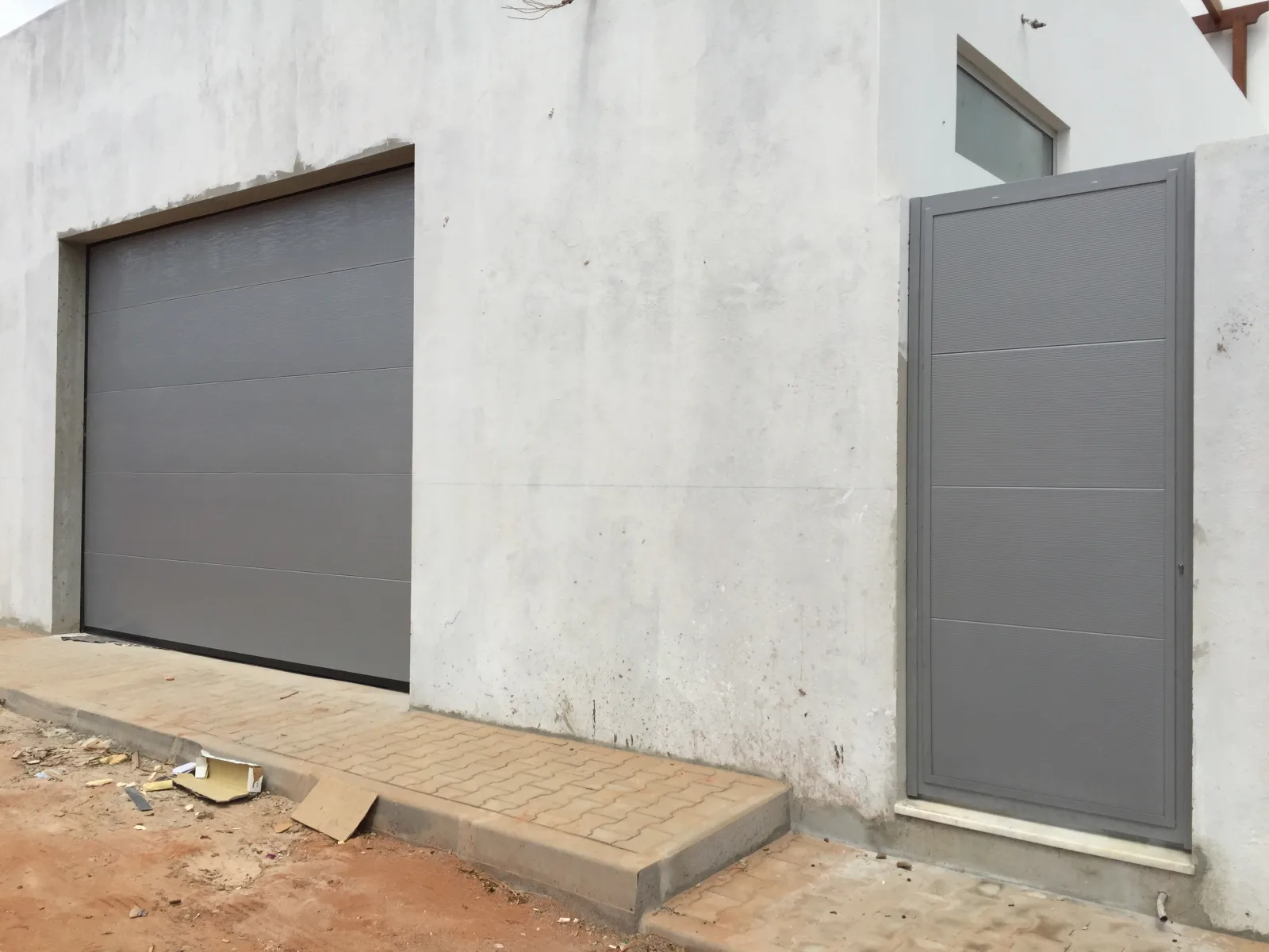 Porta pedonal metálica cinzenta instalada numa fachada rebocada — Grupo KEFE, Luanda.