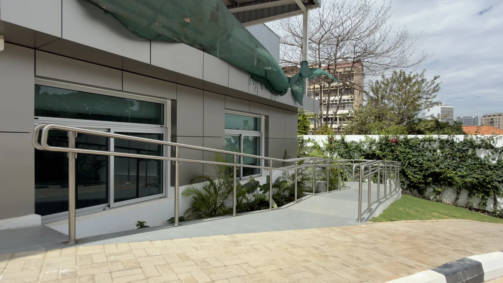 Corrimão de aço inoxidável ao longo de uma rampa pavimentada, junto a um edifício — Grupo KEFE, Luanda.