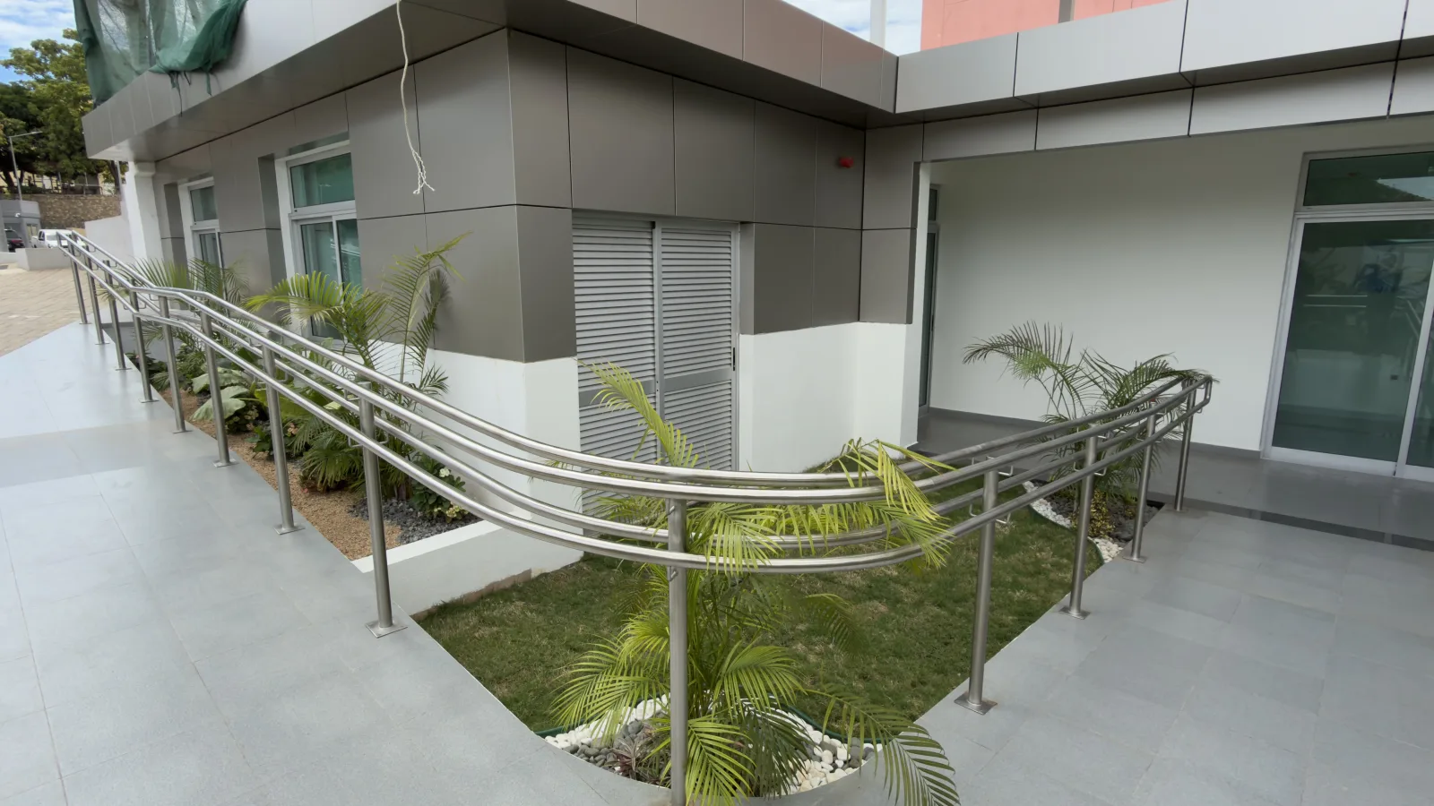 Guarda e corrimão curvos em aço inoxidável ao longo de uma rampa, num pátio residencial — Grupo KEFE, Luanda.