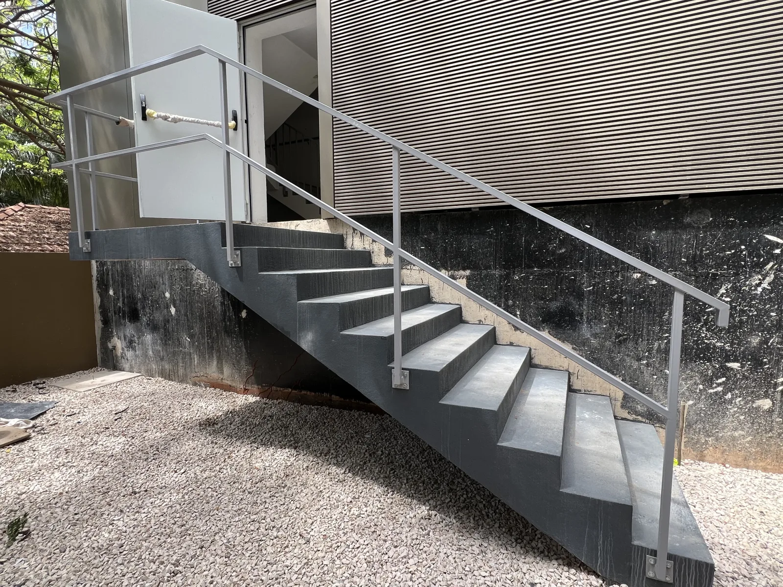 Escada metálica exterior com guarda e corrimão de aço inoxidável, junto a uma fachada revestida a chapa perfurada — Grupo KEFE, Luanda.