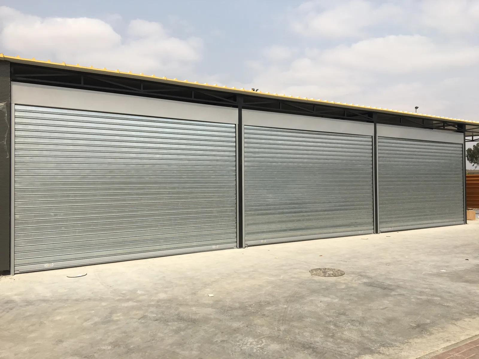 Três grades de enrolar cegas claras lado a lado numa frente comercial — Grupo KEFE, Luanda.